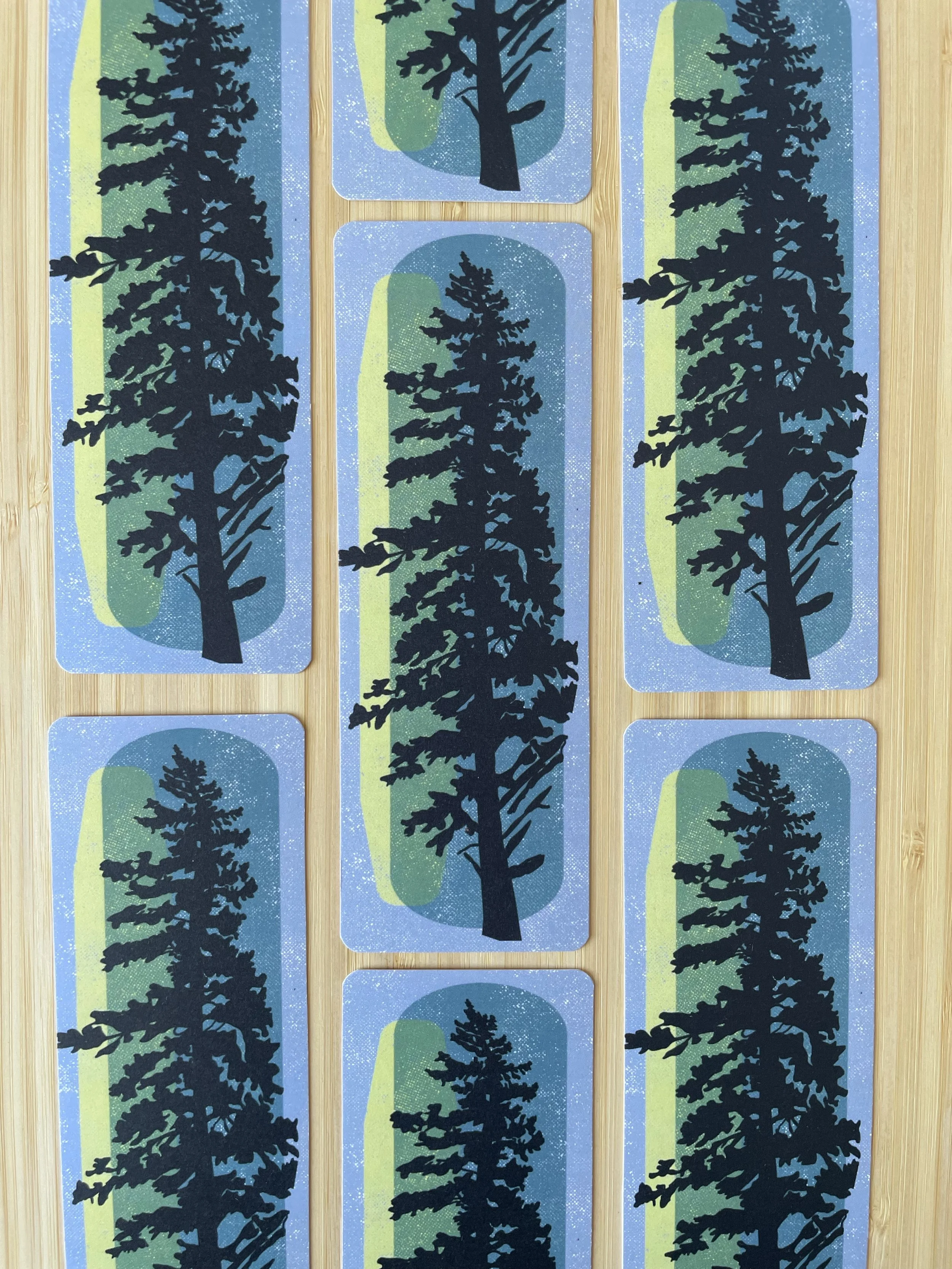 A collection of evergreen bookmarks sits grid style atop of a wooden surface.