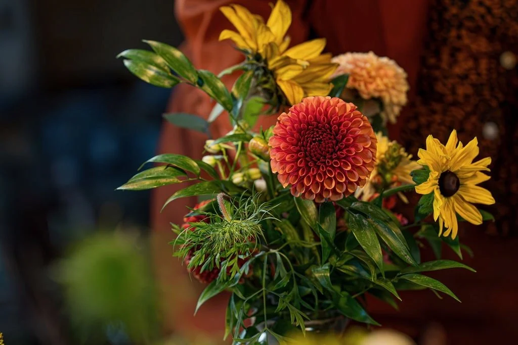 A bouquet of colourful flowers including orange dahlias, yellow sunflowers, and foliage for a celebration of life ceremony