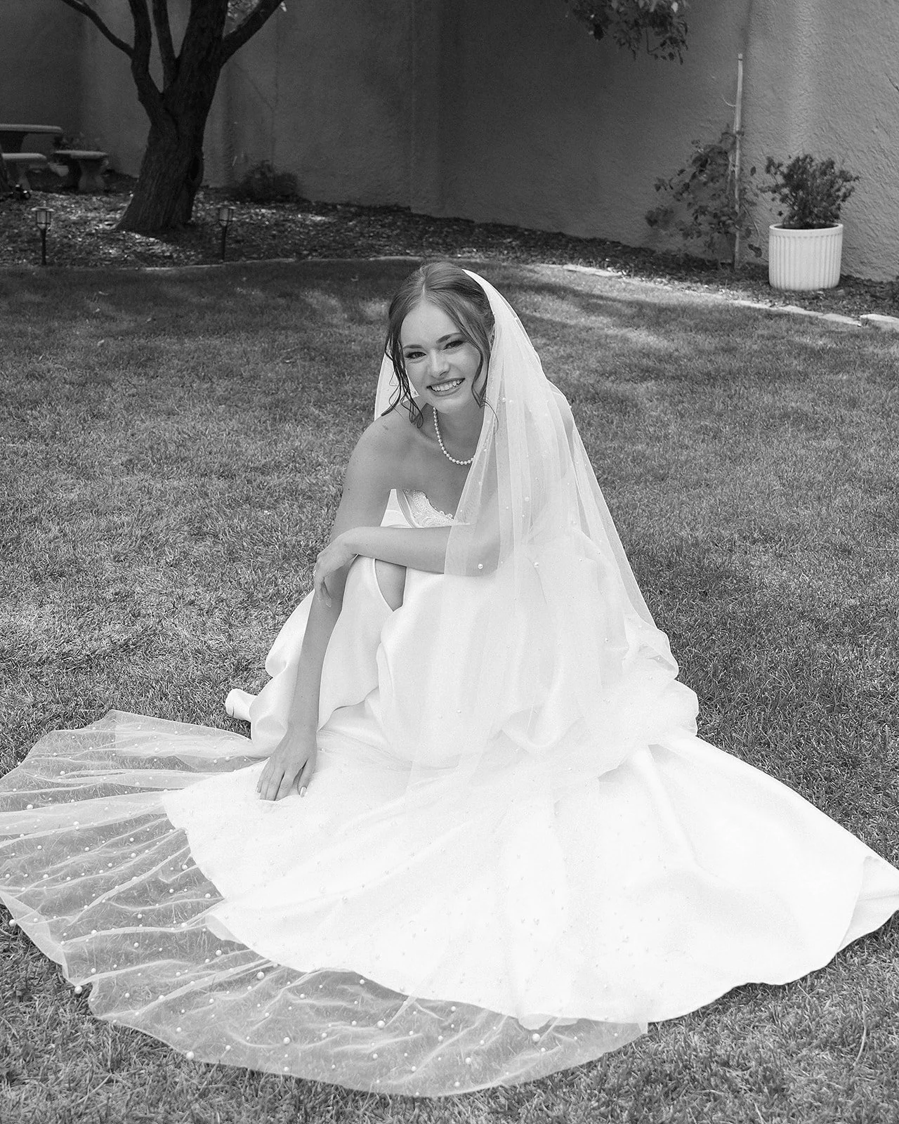 A woman in a wedding dress sitting on the grass with a smile
