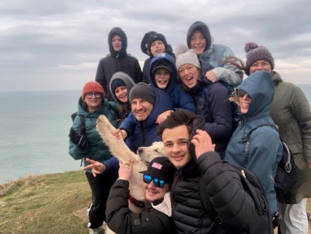 Group of people smiling on a cliffside with a dog in winter clothing.