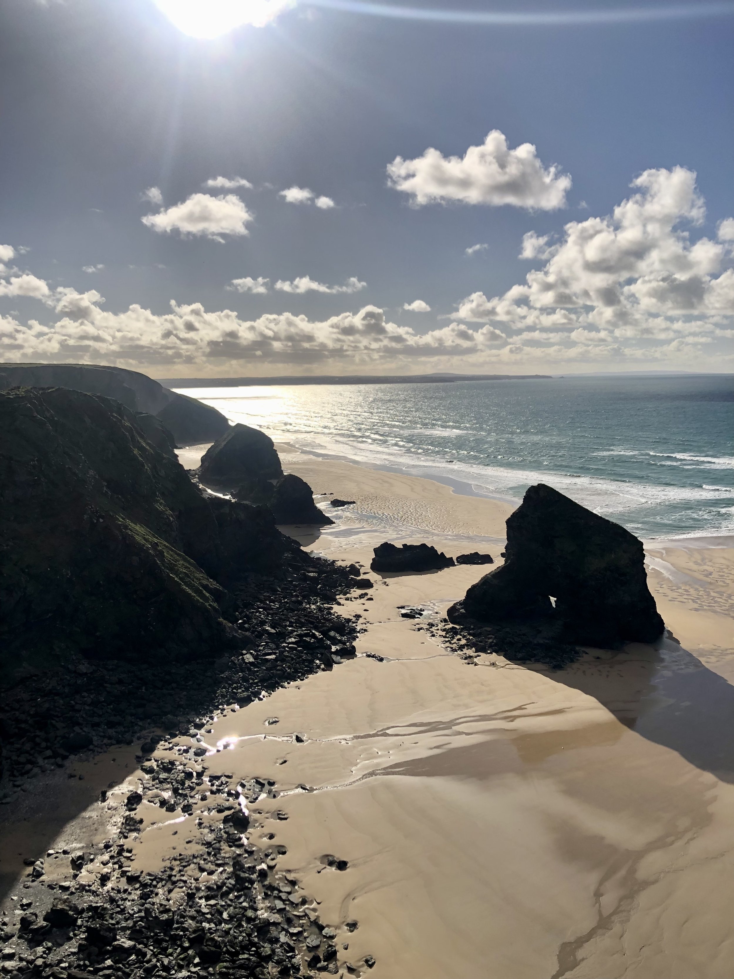 Scenic coastal landscape with large rocks and sandy beach under a sunny sky with clouds.