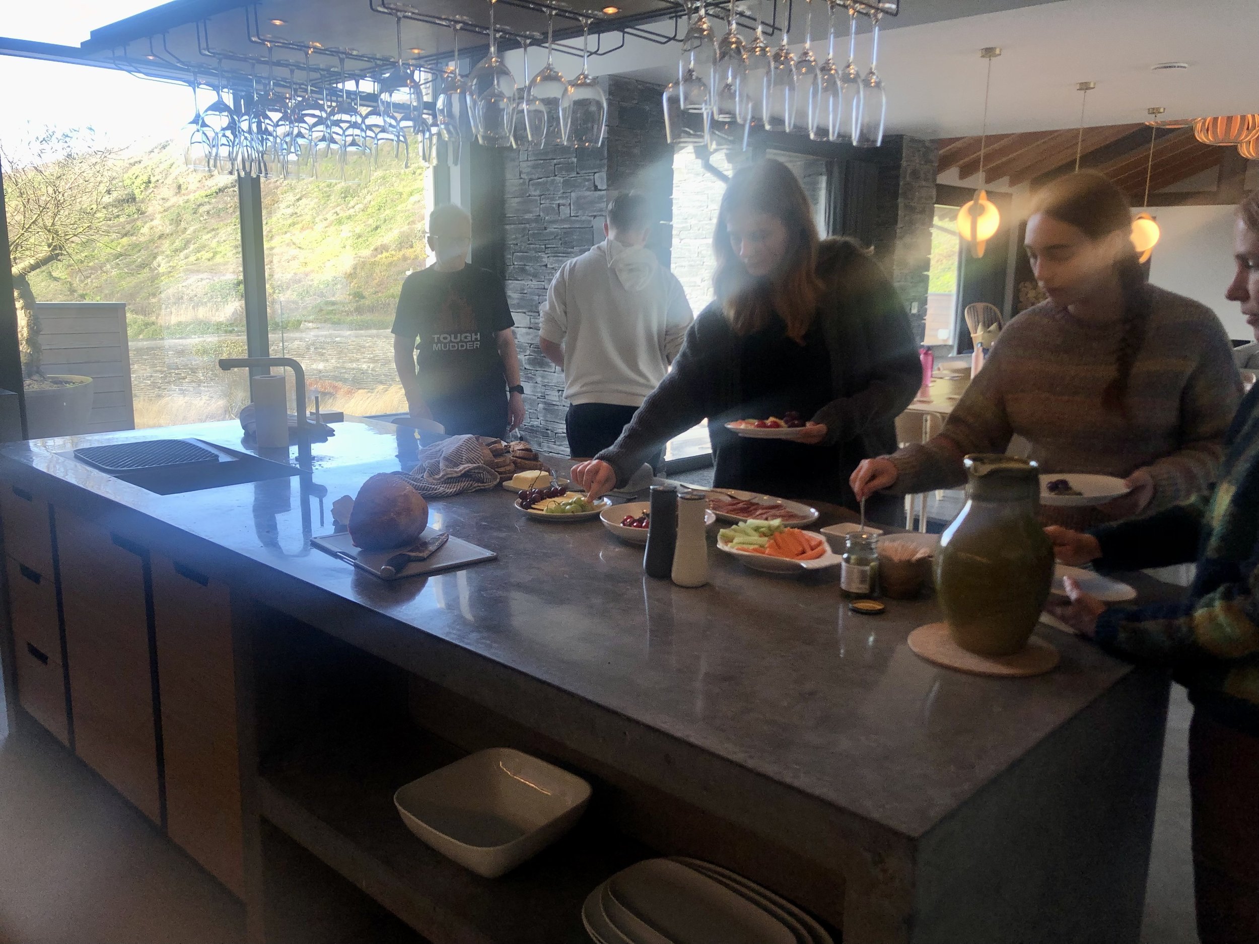 Group of people standing around a kitchen island with food and drinks, preparing plates