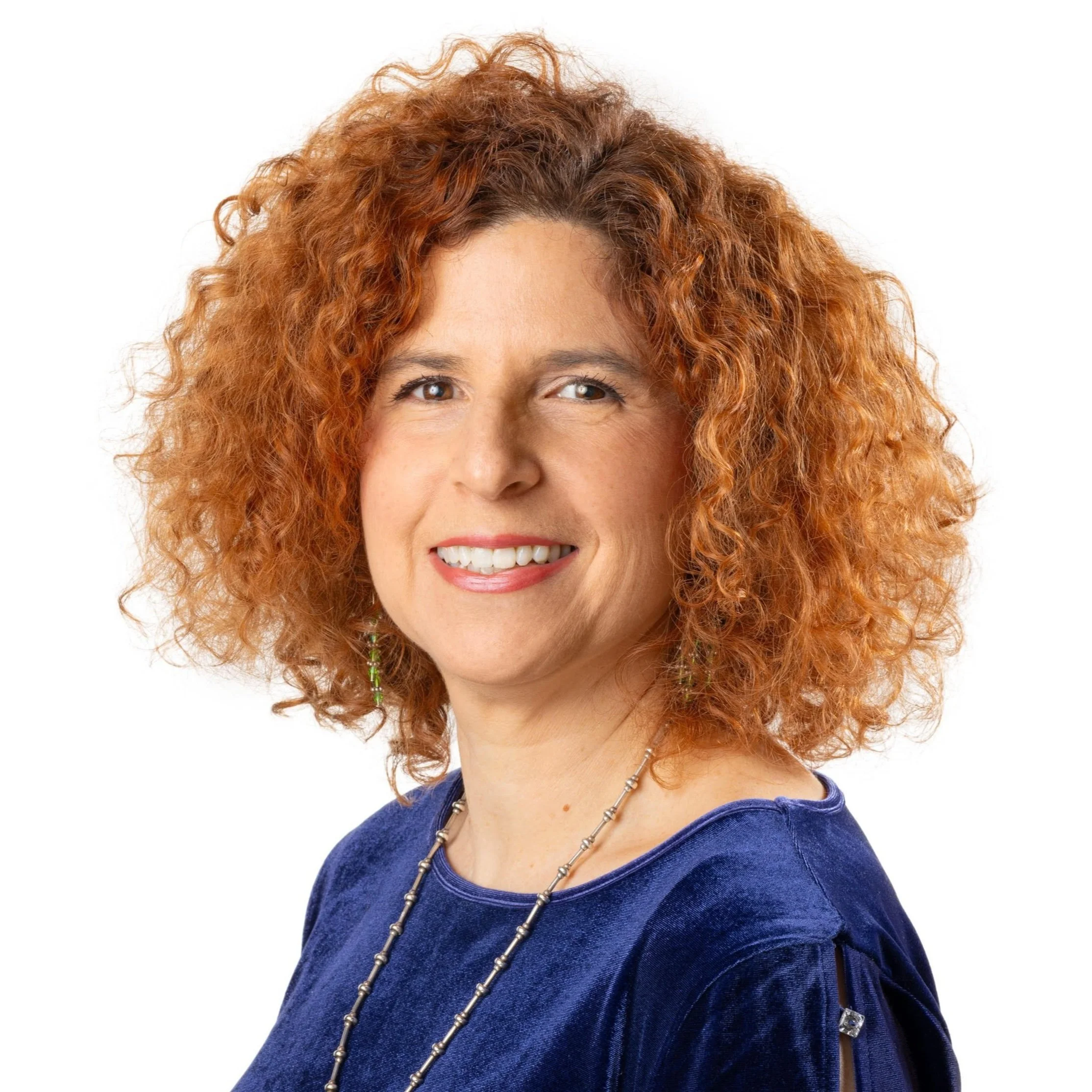 Chicago parenting therapist with curly red hair smiling, wearing a blue velvet top and jewelry, against a white background.