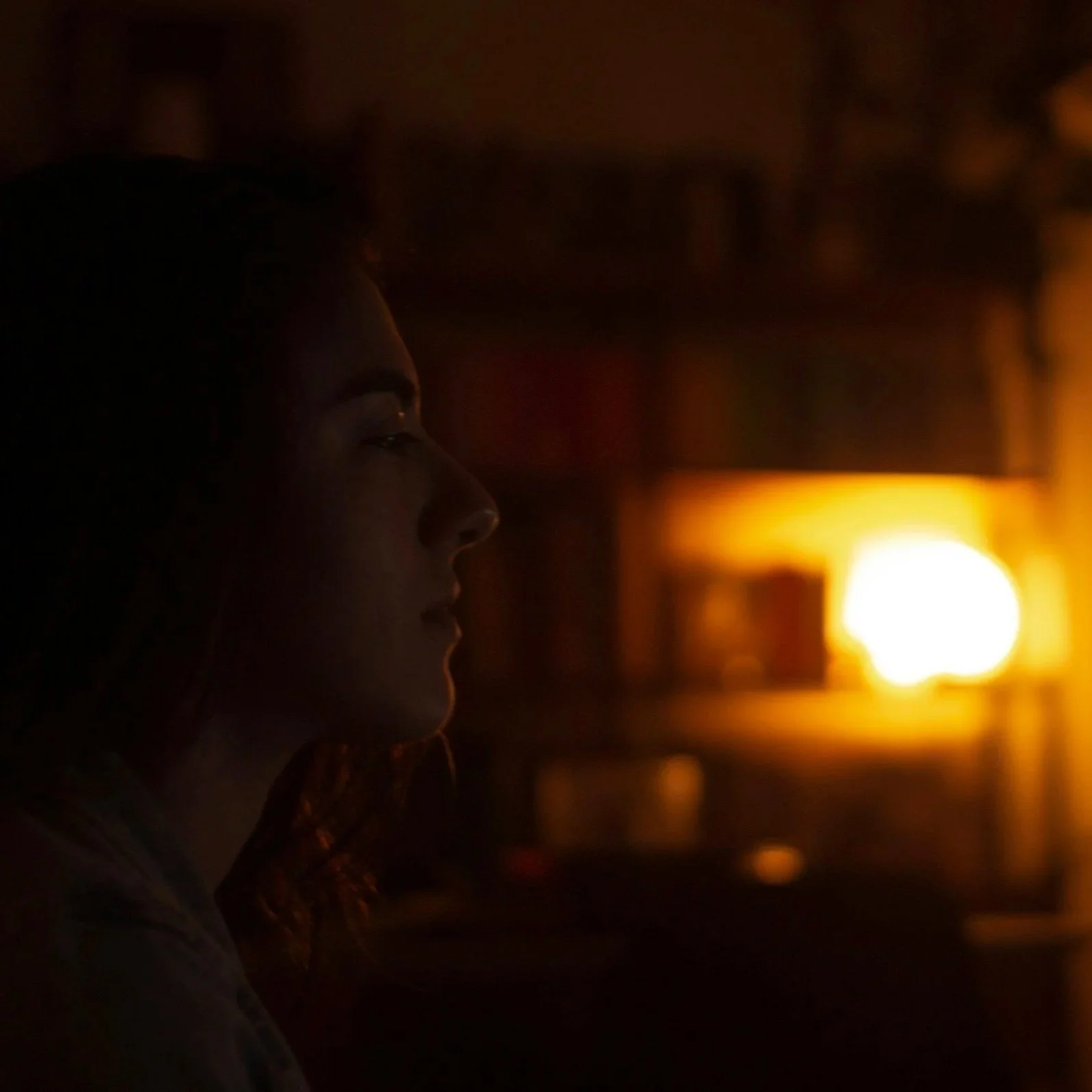 woman in dark room looking tired with light on in the background