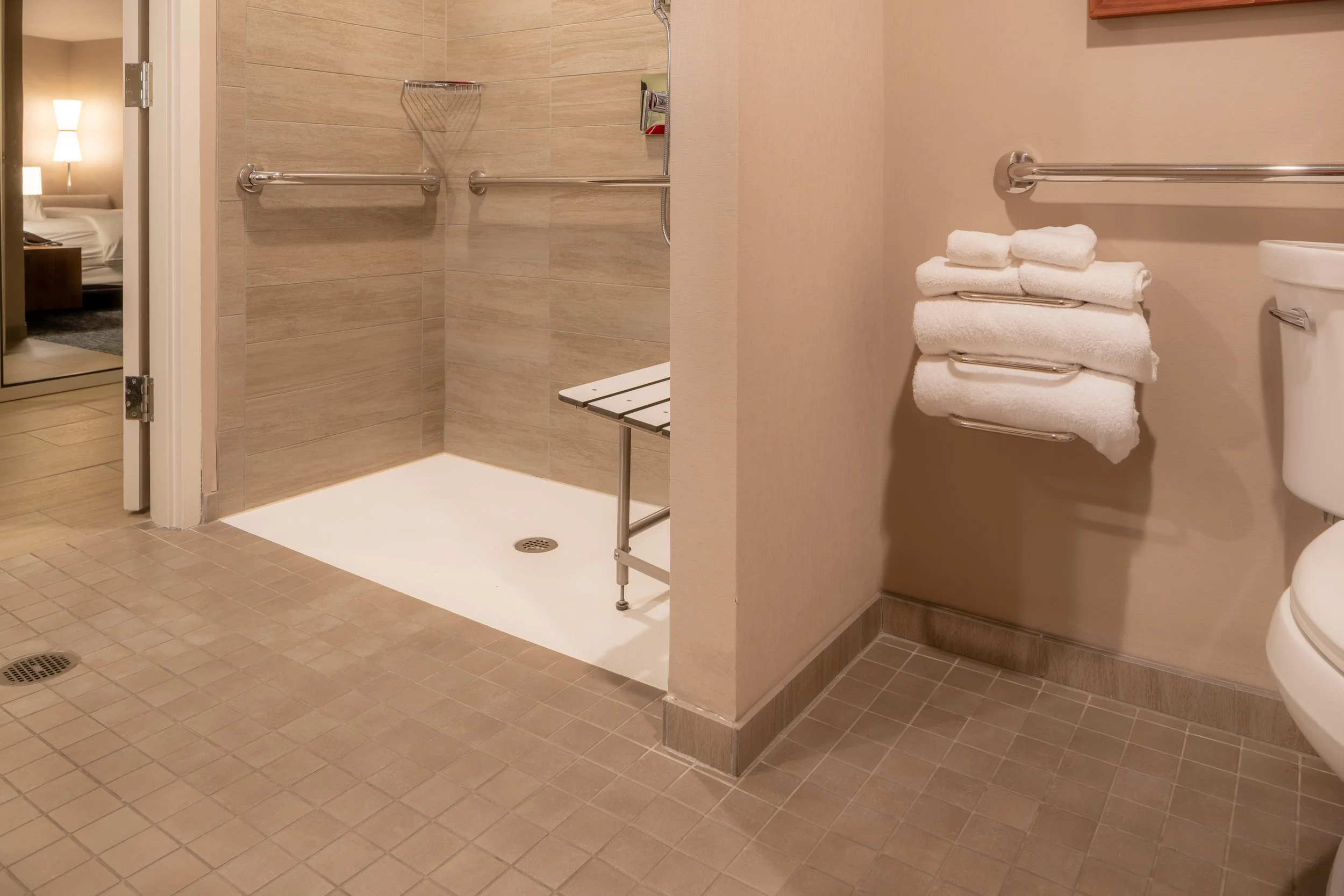modern ADA accessible bathroom with curbless shower. shower bench, towel rack and grab bars