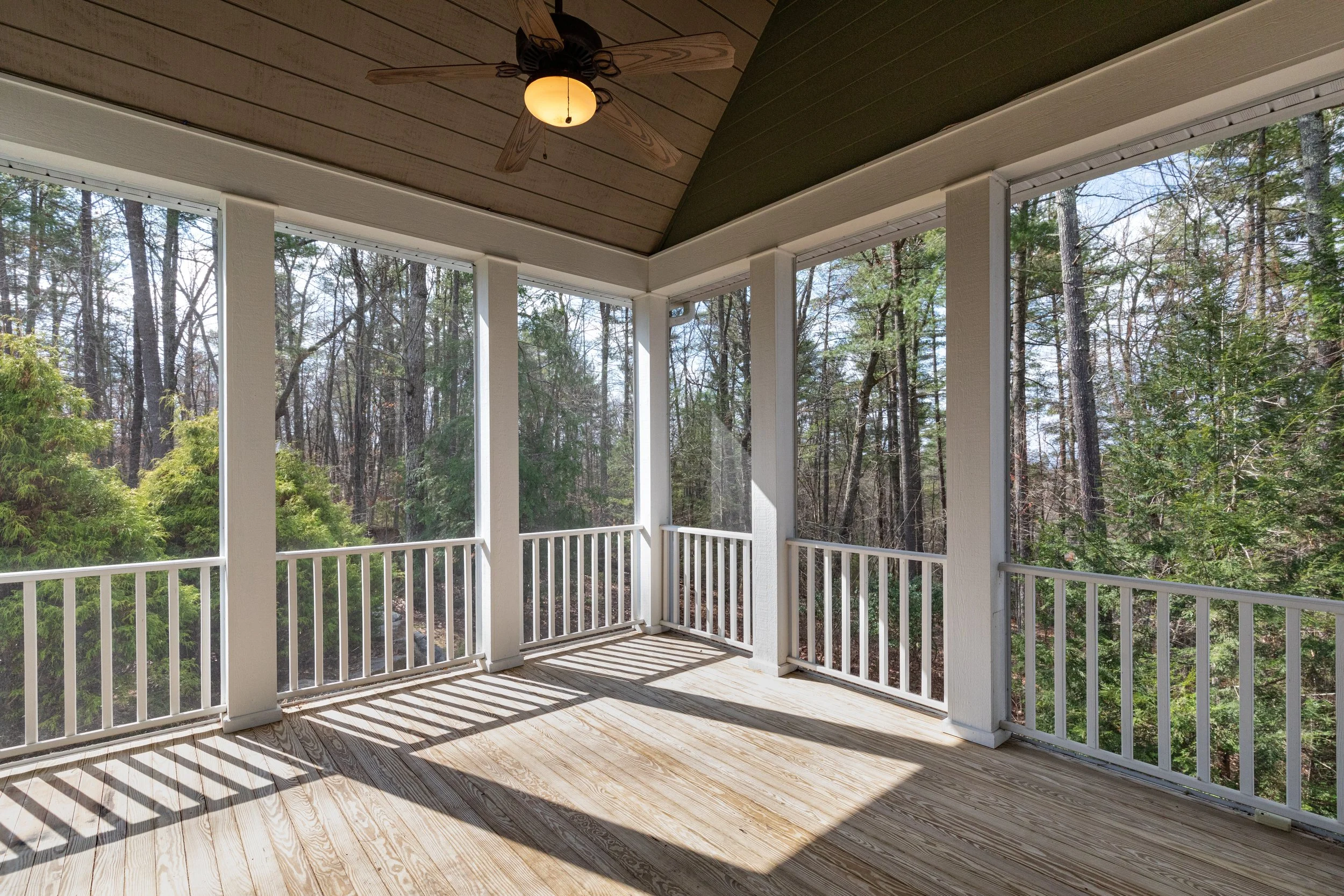Newly constructed screened porch with vaulted ceilin, ceiling fan, Westbury aluminum railing system, white composite pillars, blonde wood tone composite decking, and safety screens