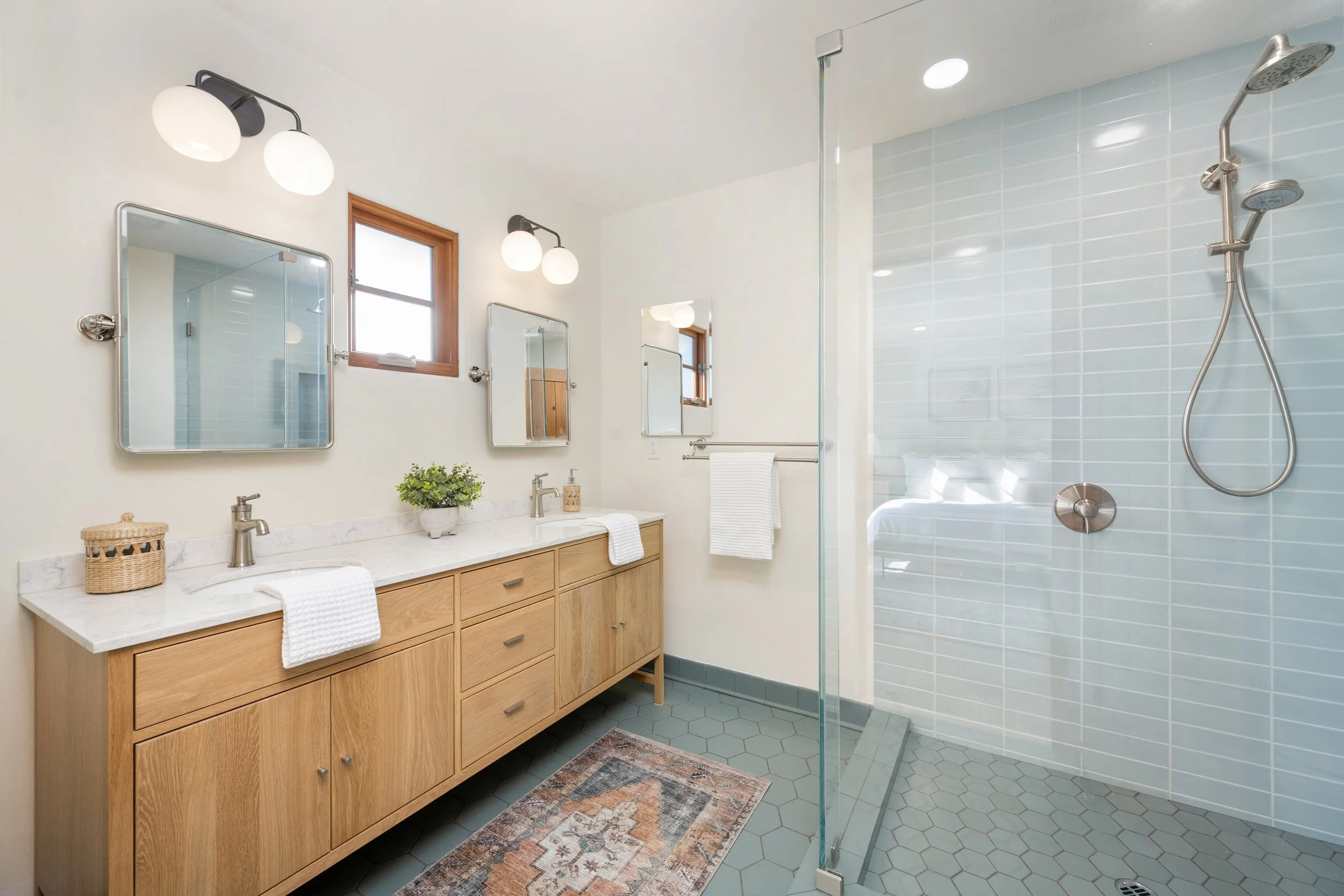 Modern bathroom remodel with full-length Euro-glass shower enclosure, speciality shower wand, natural wood floating vanity, double sink and faucet sets, tile floor and area rug