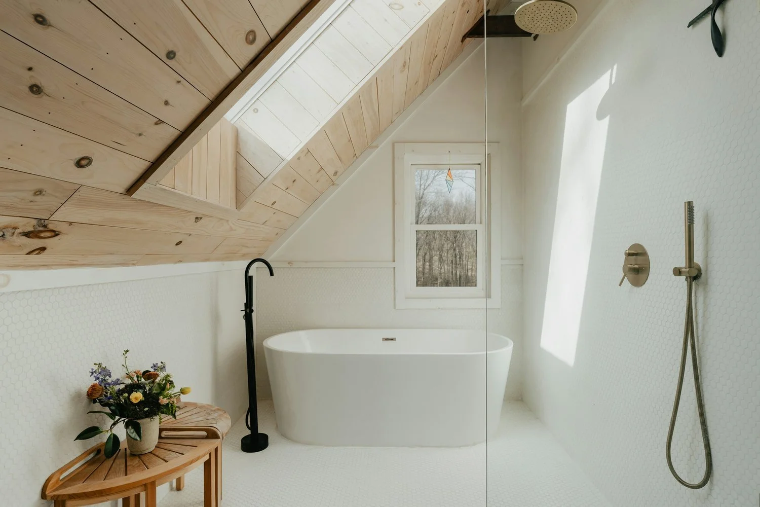 Loft bathroom with skylight, natural wood shiplap ceiling, white walls, with penny tile flooring, stand alone tub, and external stanchion faucet set