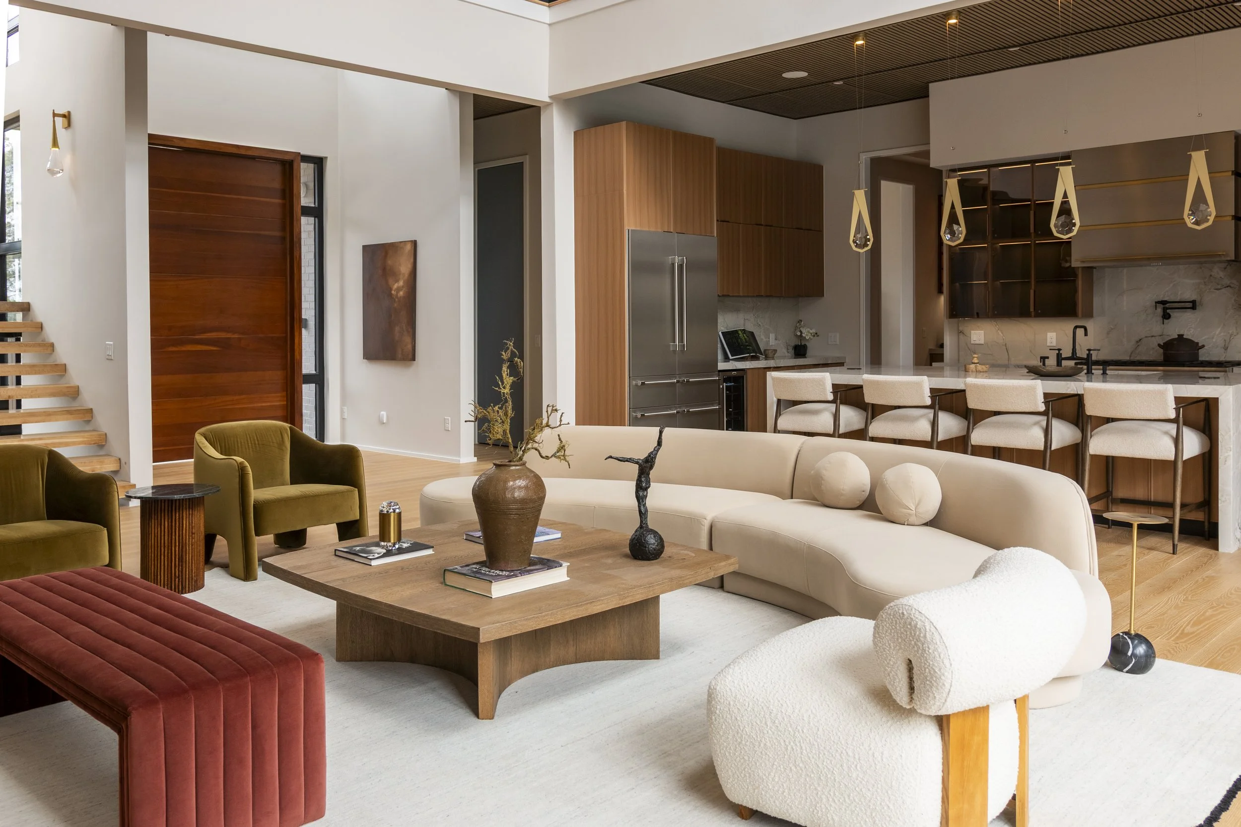 Sala de estar con paredes blancas, chimenea de ladrillo, sofá blanco con cojines, arte abstracto en la pared, ventanas con cortinas blancas, mesa de centro de madera, y accesorios decorativos.