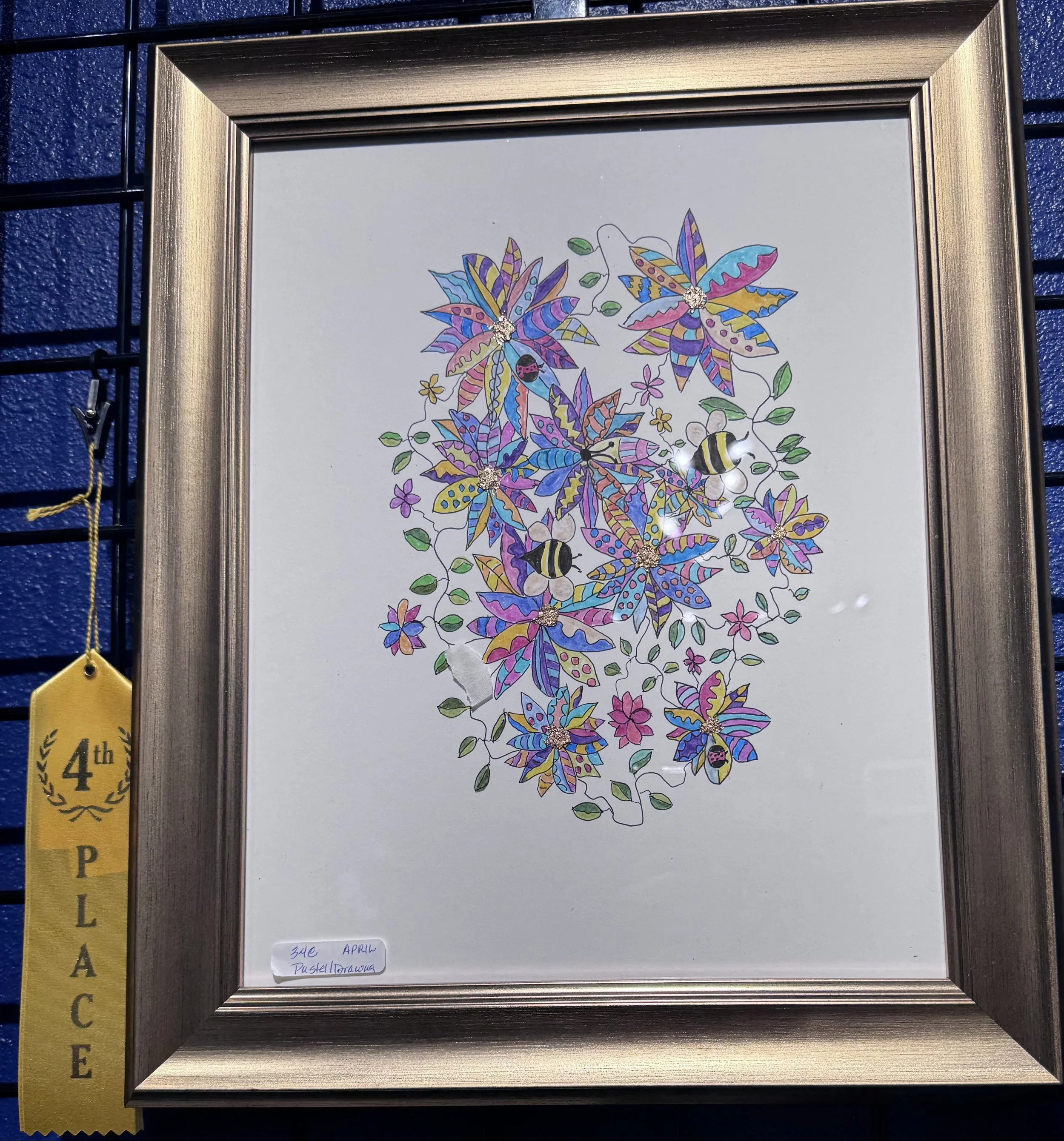 A framed drawing of colorful butterflies with flowers, leaves, and ladybugs on a white background, displayed on a black wire grid.
