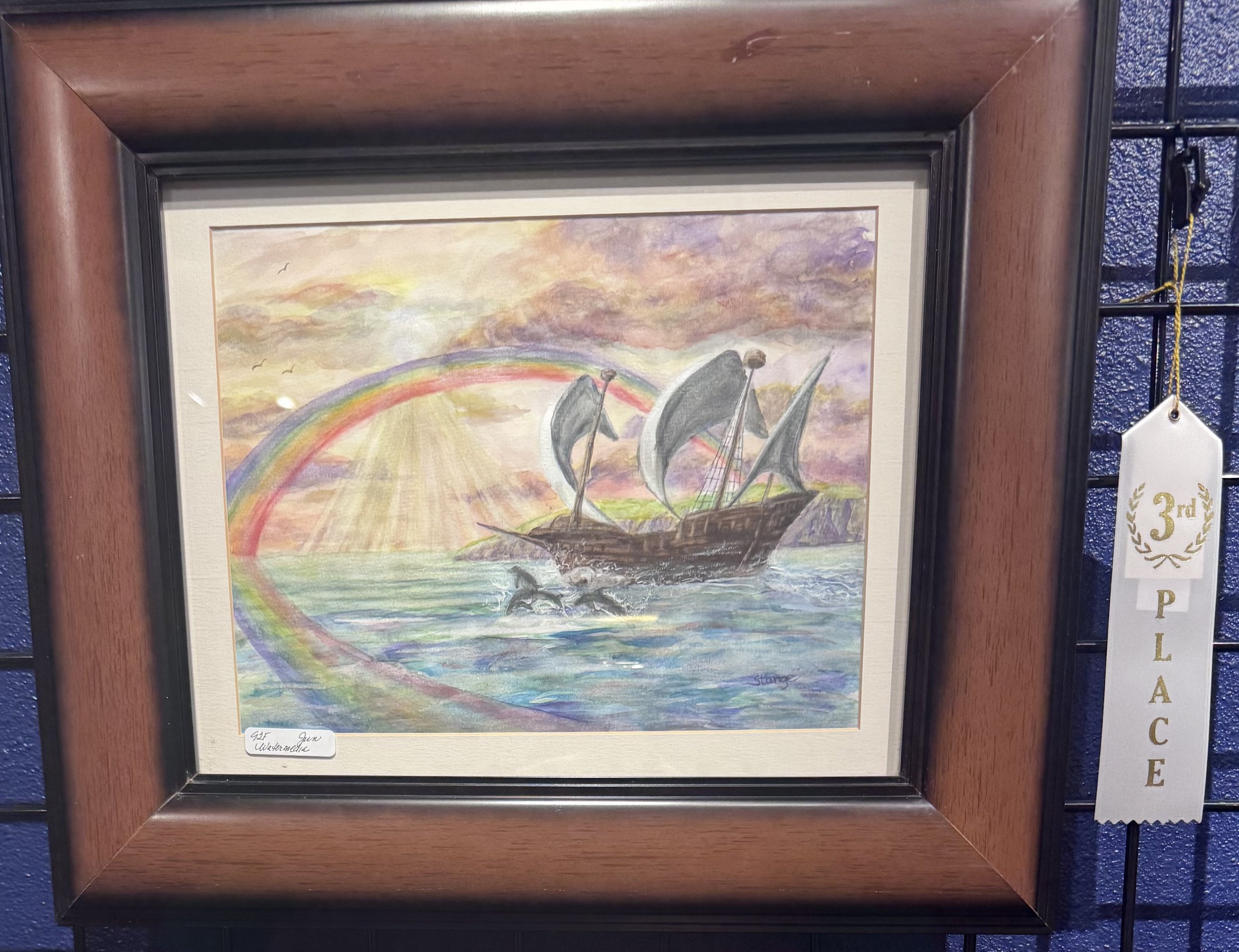Watercolor painting of four ships sailing on water under a cloudy sky with rainbow in the background, framed in a wooden frame with a third-place ribbon attached to the right side.