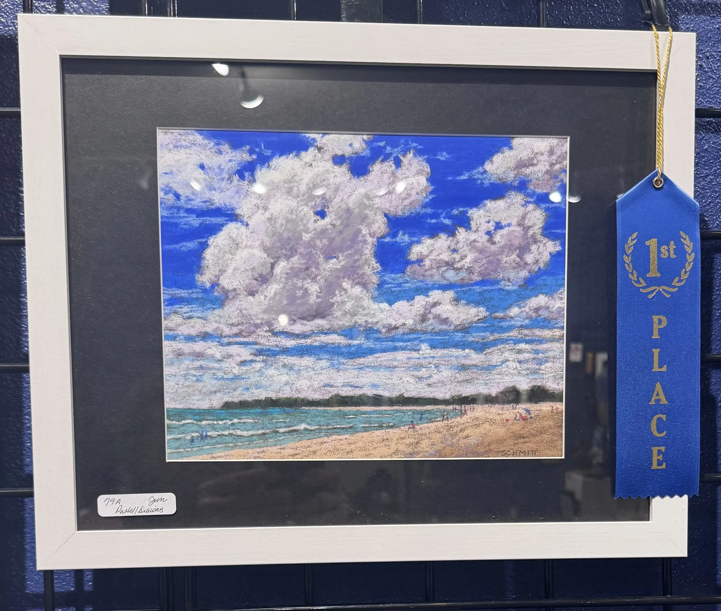 Painting of the sky with clouds in pastel colors displayed in a white frame.