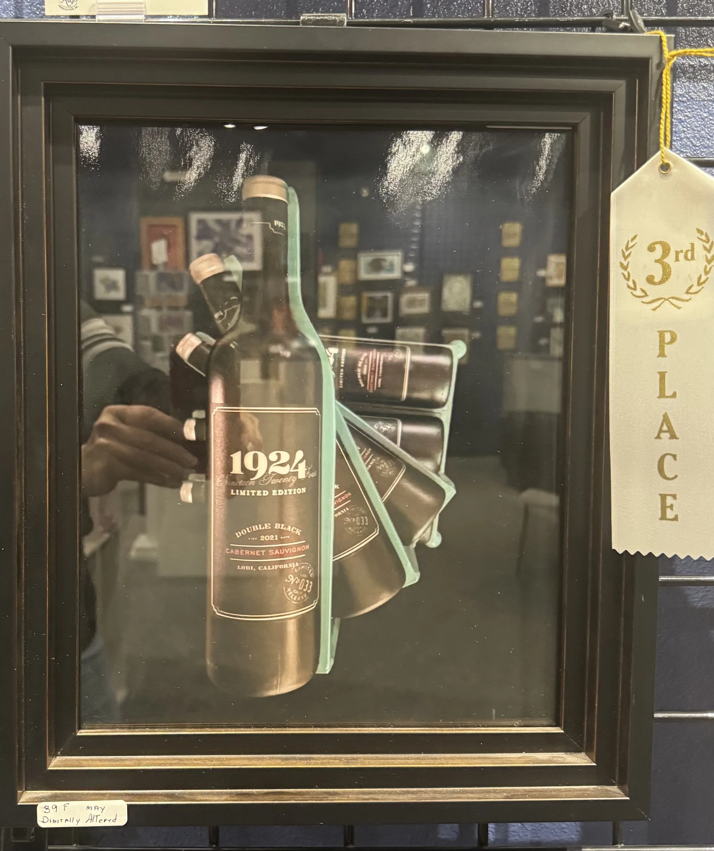 A black display case with a glass front containing several bottles of wine or liquor, including a limited edition 1924 vintage Cabernet Sauvignon from Lodi, California. There are behind-the-scenes reflections of a person's hand holding a phone and a 