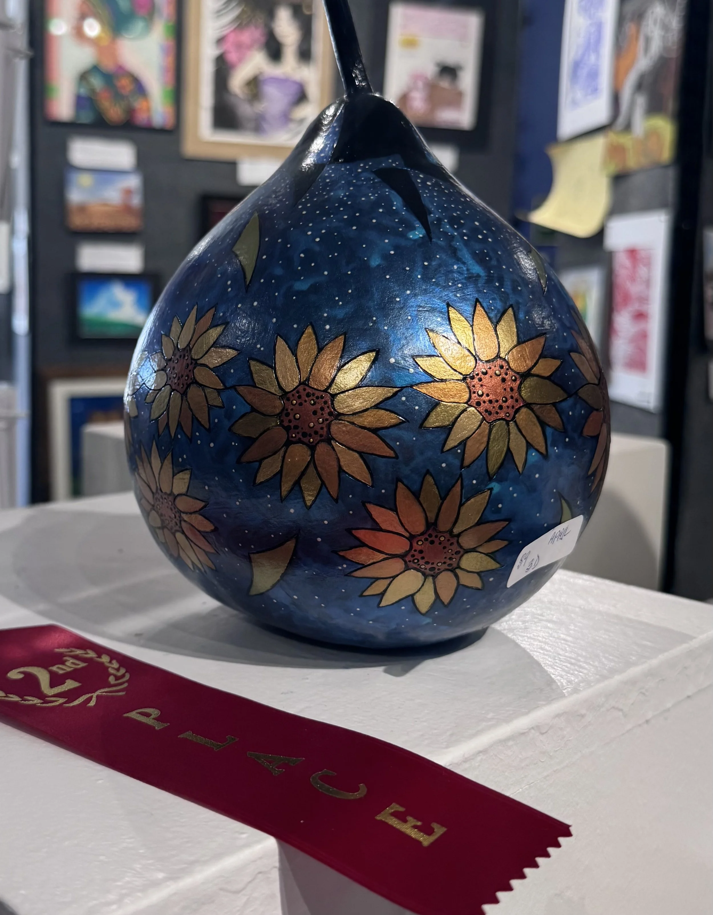 Ceramic vase decorated with sunflowers and starry night sky pattern, displayed on a white pedestal at an art show.