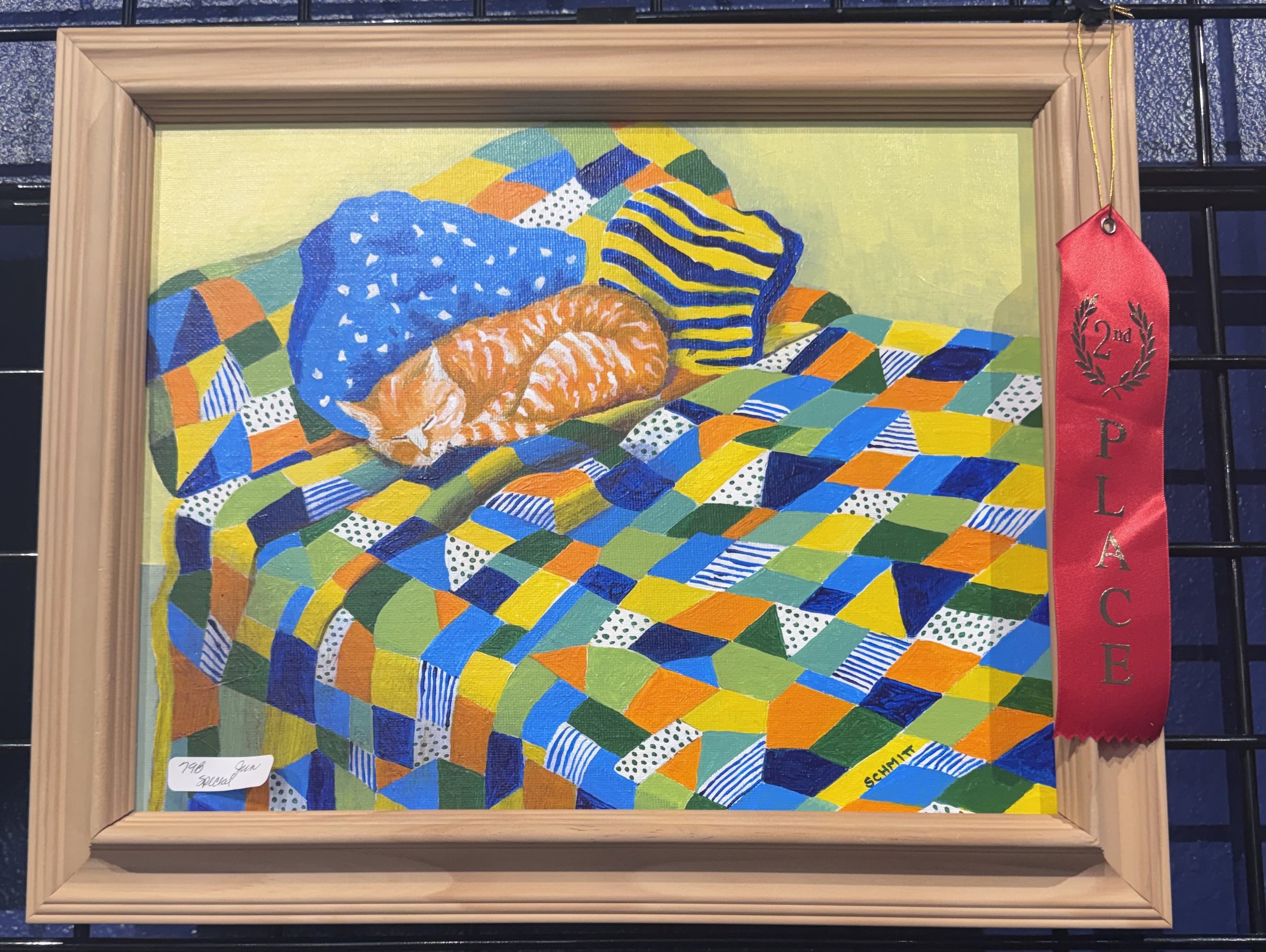 Colorful abstract artwork of a cat lying on a patchwork quilt, framed and awarded second place ribbon.