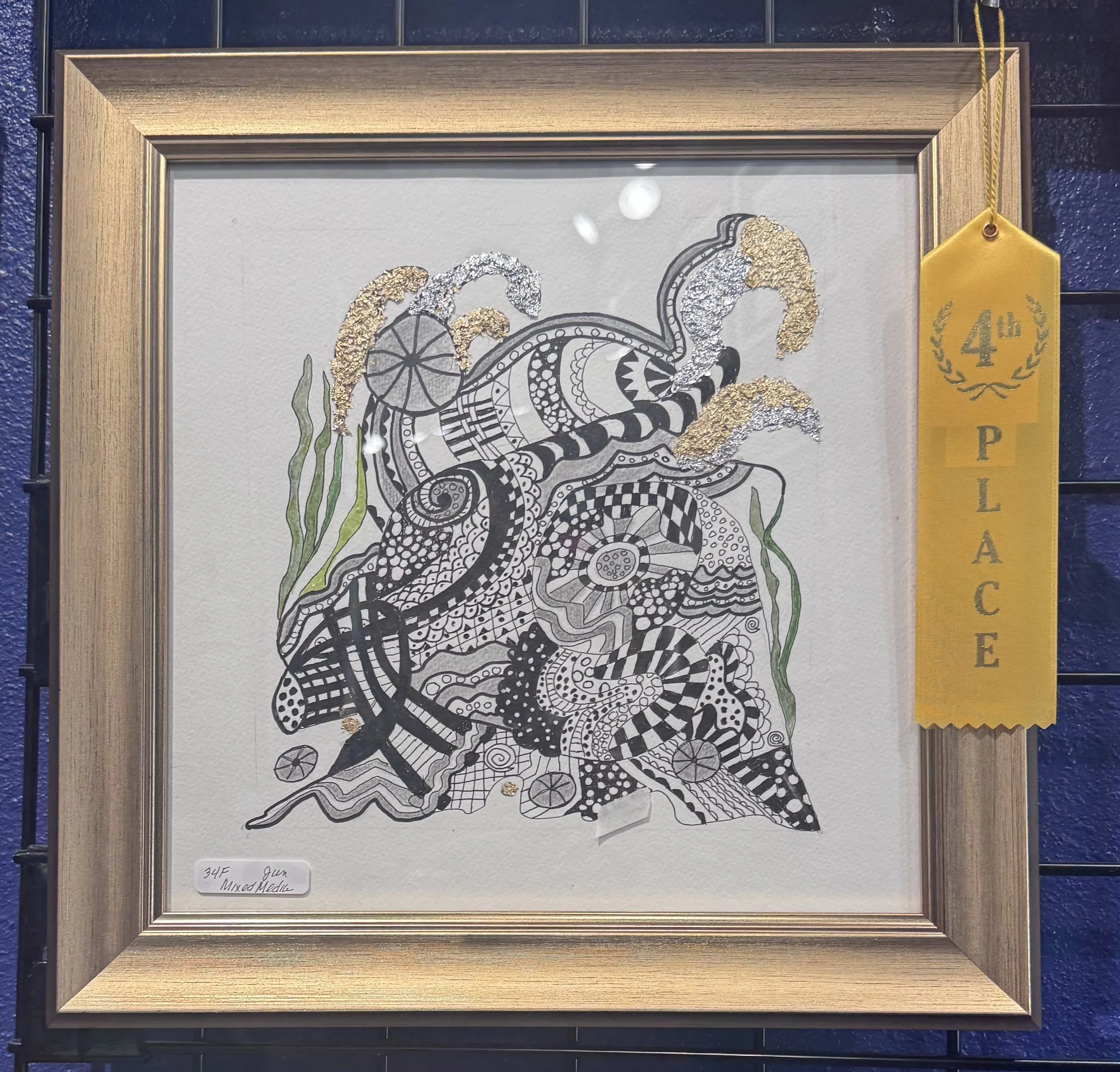 Artwork of a snake in a black and white pattern, highlighted with gold and silver textured accents, framed in a wooden frame, with a yellow ribbon tag on the right side that reads "41st" and "PB".