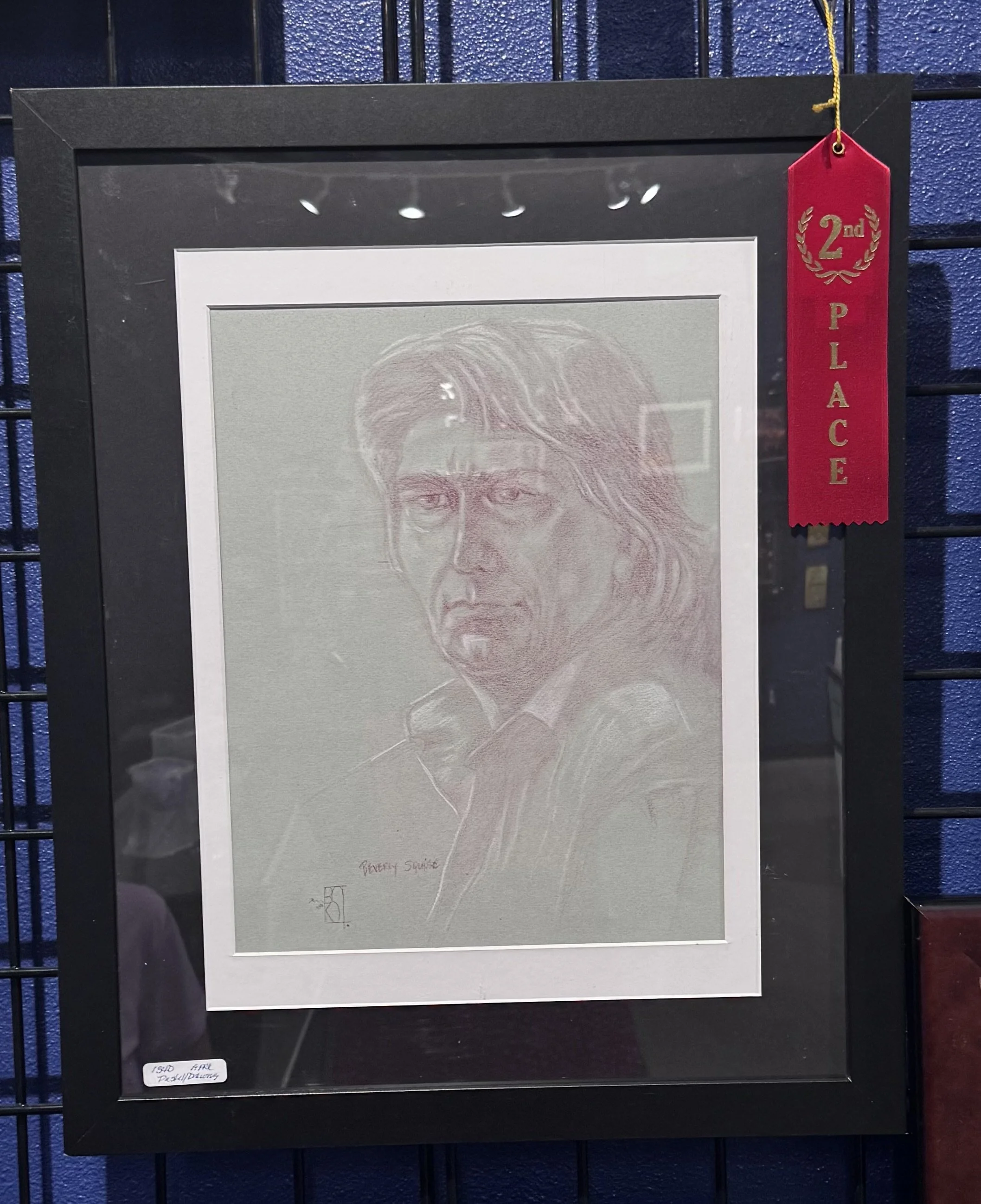 Framed pencil sketch of a person's face with long hair, labeled 'Beauty Source'. The frame has a red ribbon tag marked '2nd Place' hanging from the top right corner.