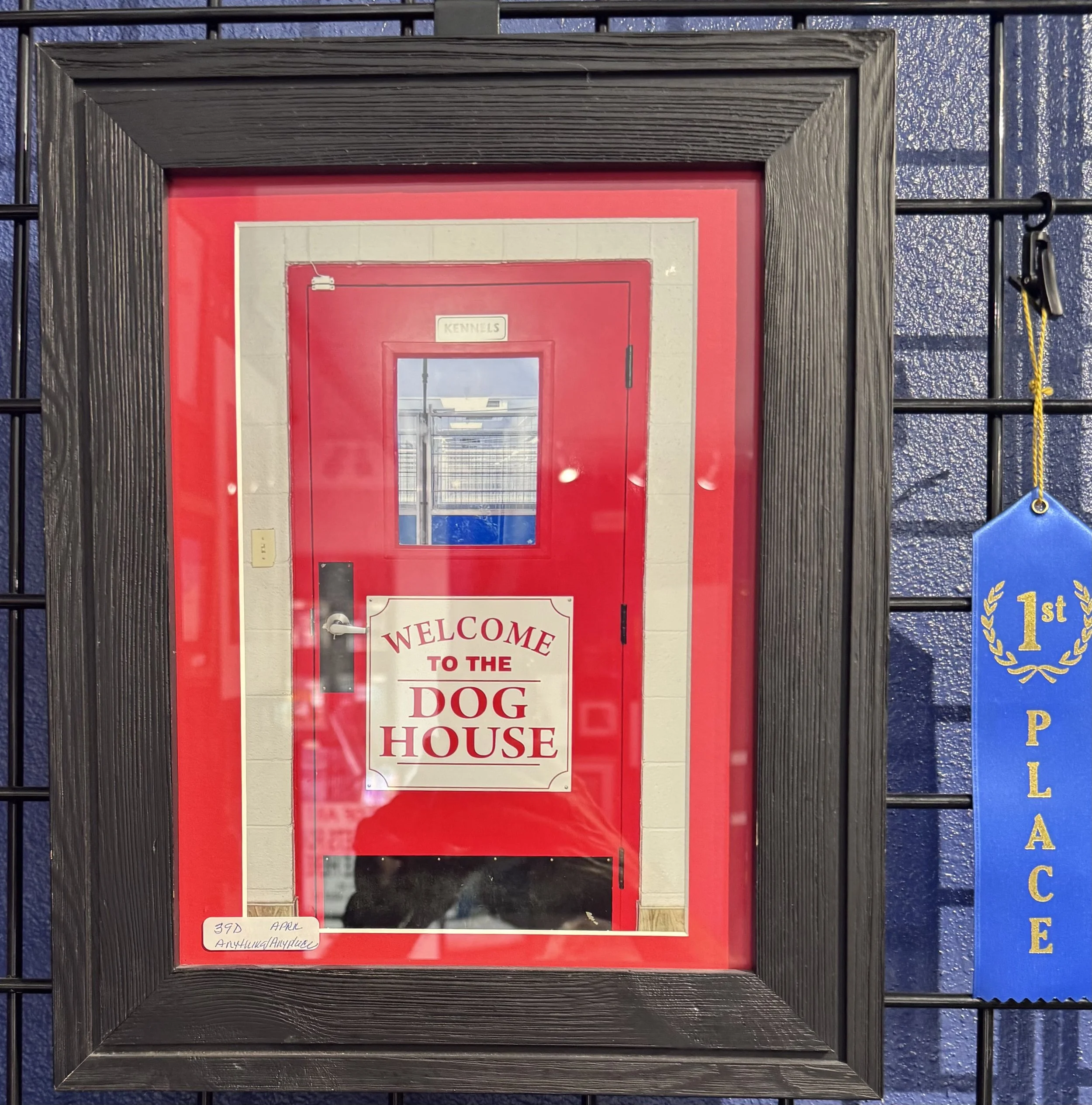 A sign in a red frame on a wall of a dog house with the text "Welcome to the Dog House" and a window in the middle.