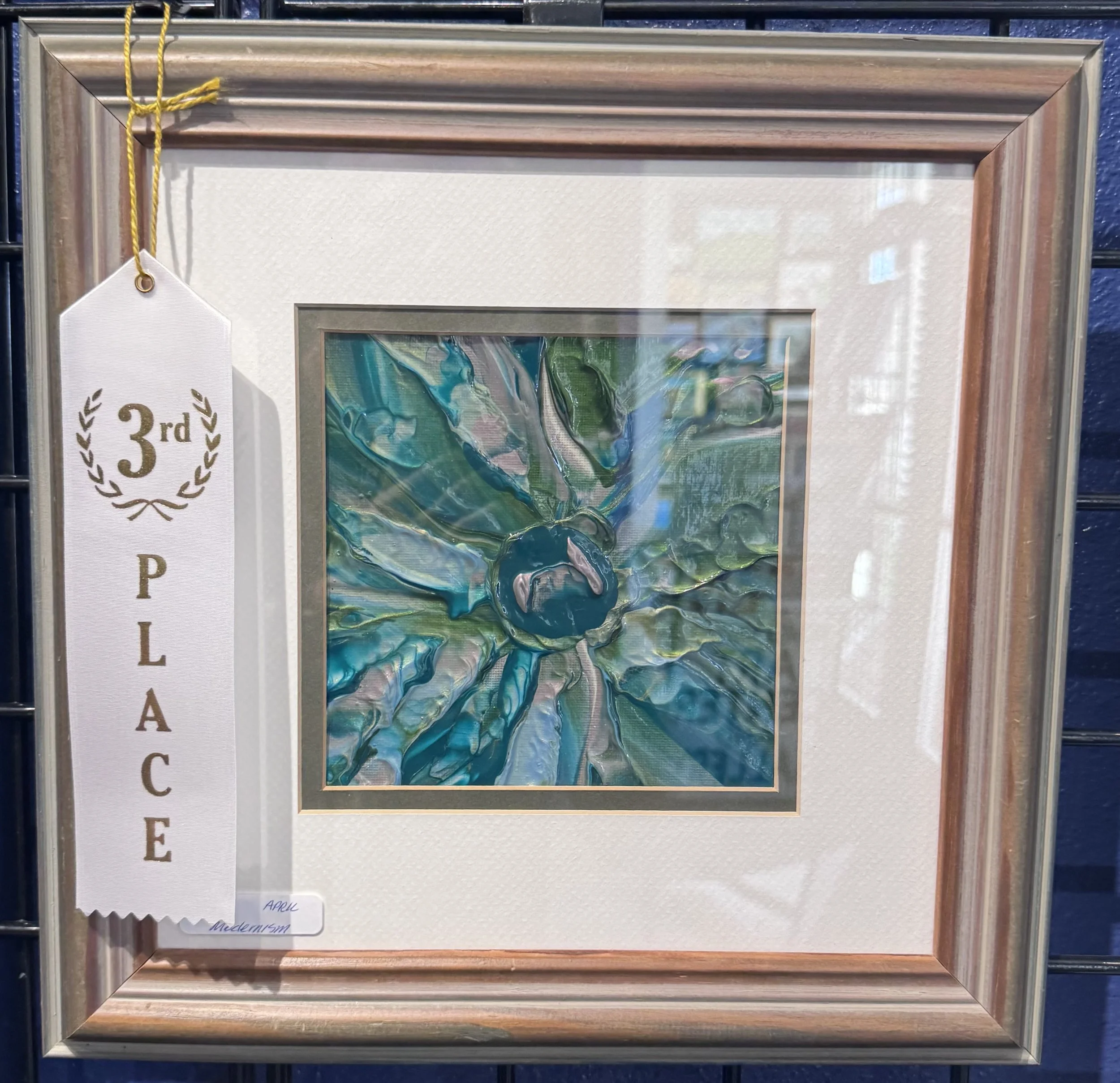 Framed abstract artwork with shades of blue, green, and pink, with a white ribbon indicating third place in an art competition.