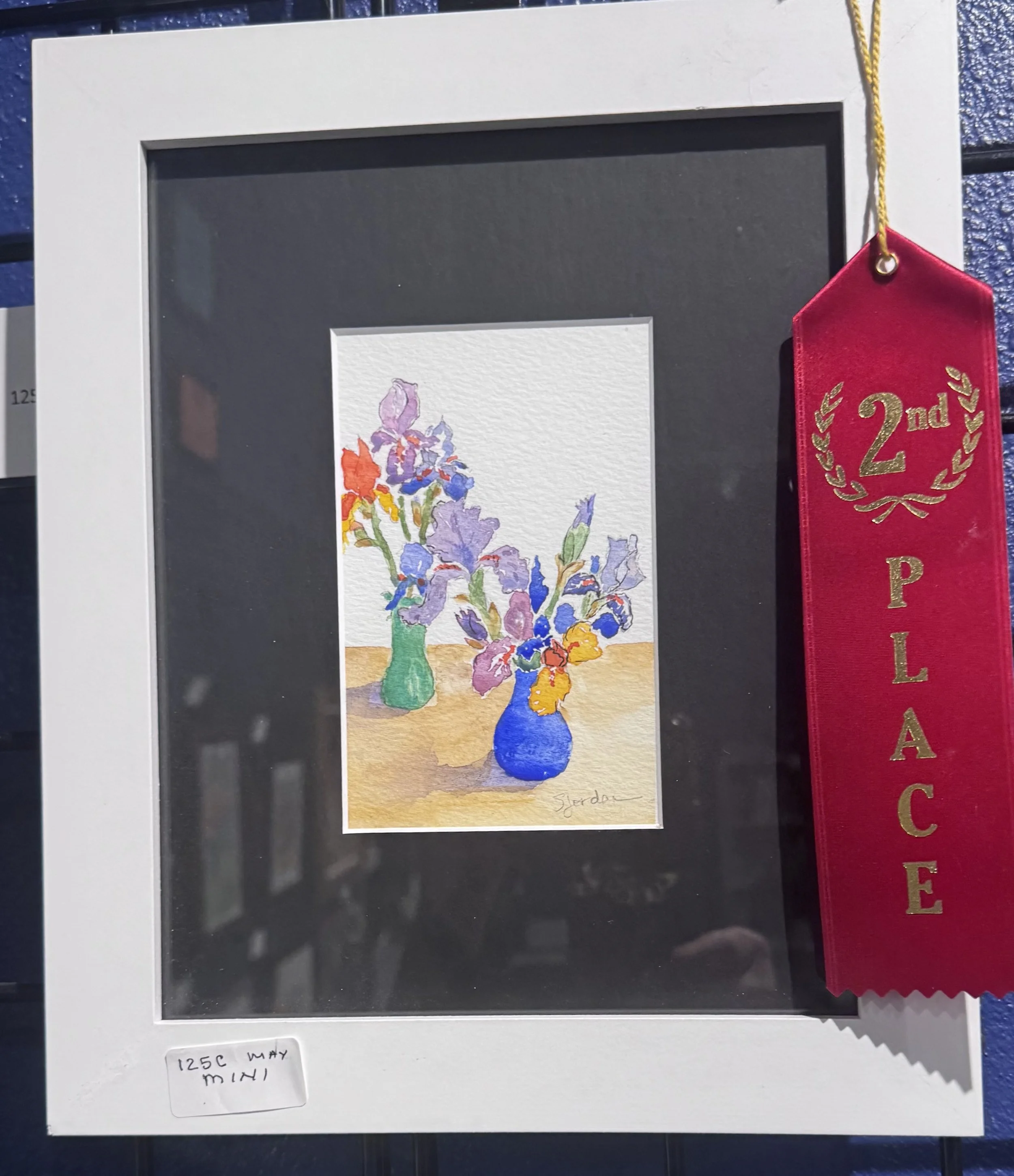 A watercolor painting of three vases filled with iris flowers, signed by the artist "Snyder" at the bottom right. The image is displayed in a handmade gift frame with a black mat background, accompanied by a red ribbon ribbon indicating a second plac