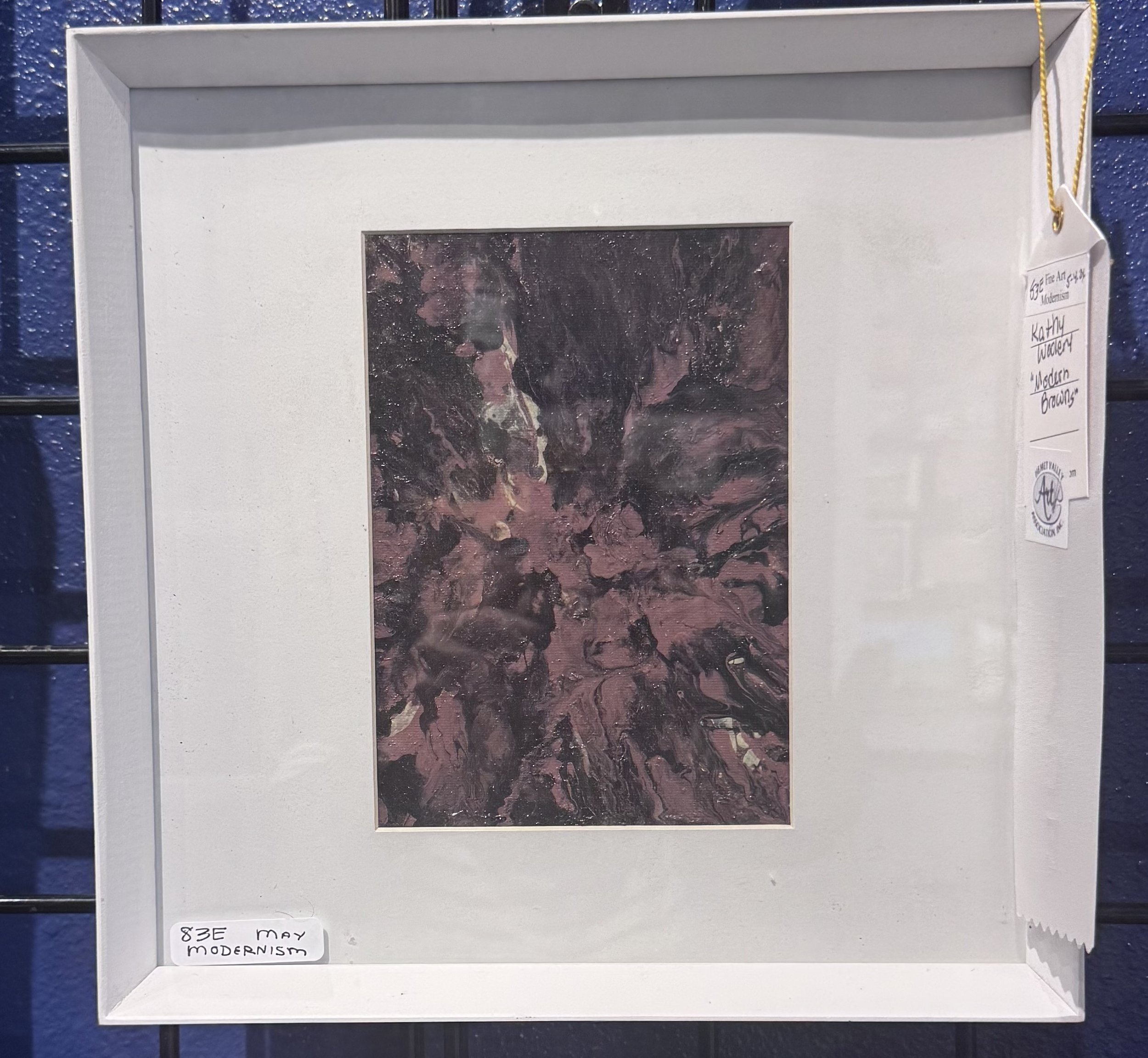 Close-up of an abstract artwork with dark pink, black, and white swirls, titled 'Modern Brows' by Kathy Tucker, displayed in a white shadow box frame.