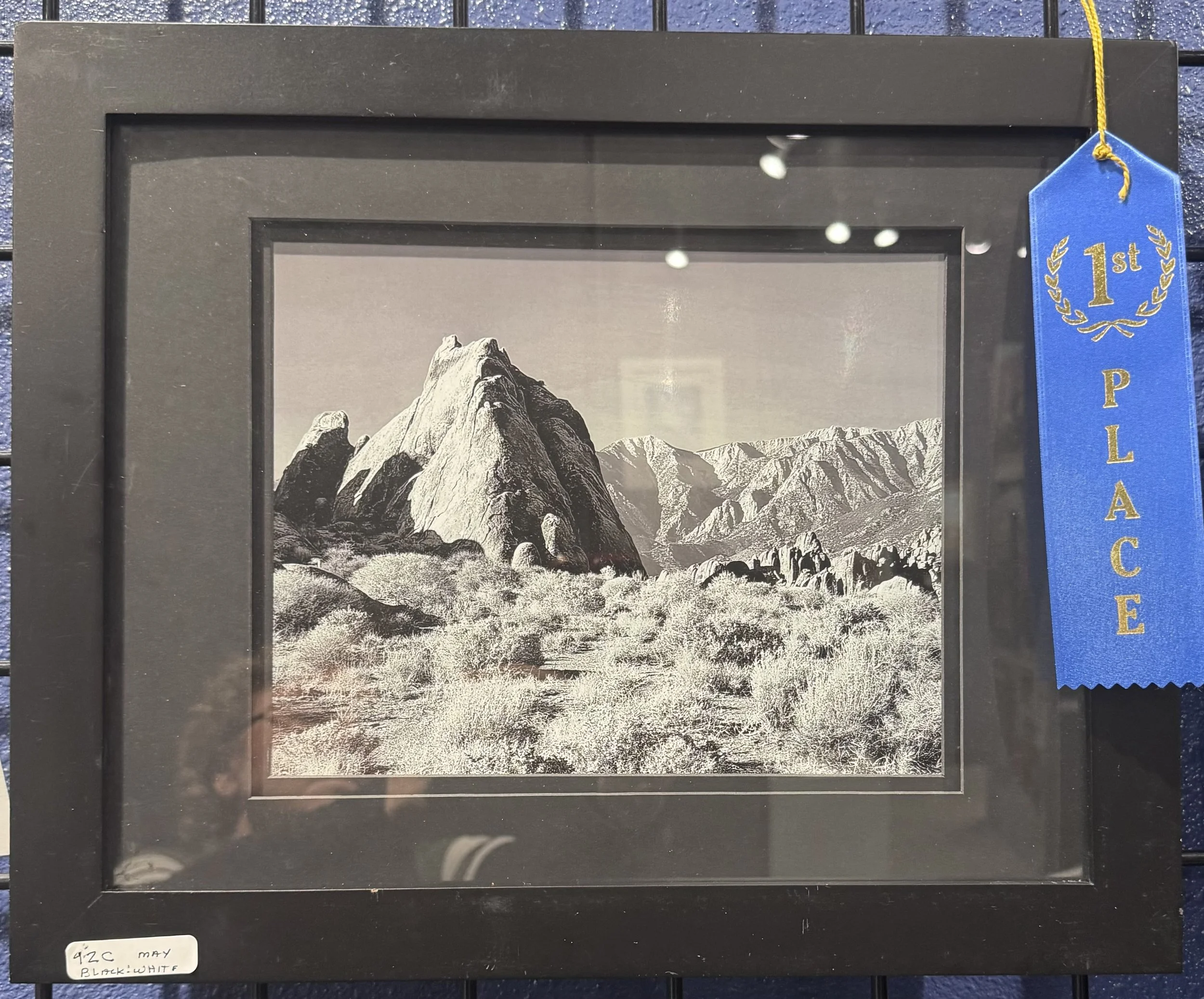 Black and white photograph of a mountain with rocky peaks under a cloudy sky, framed and displayed as an art piece.