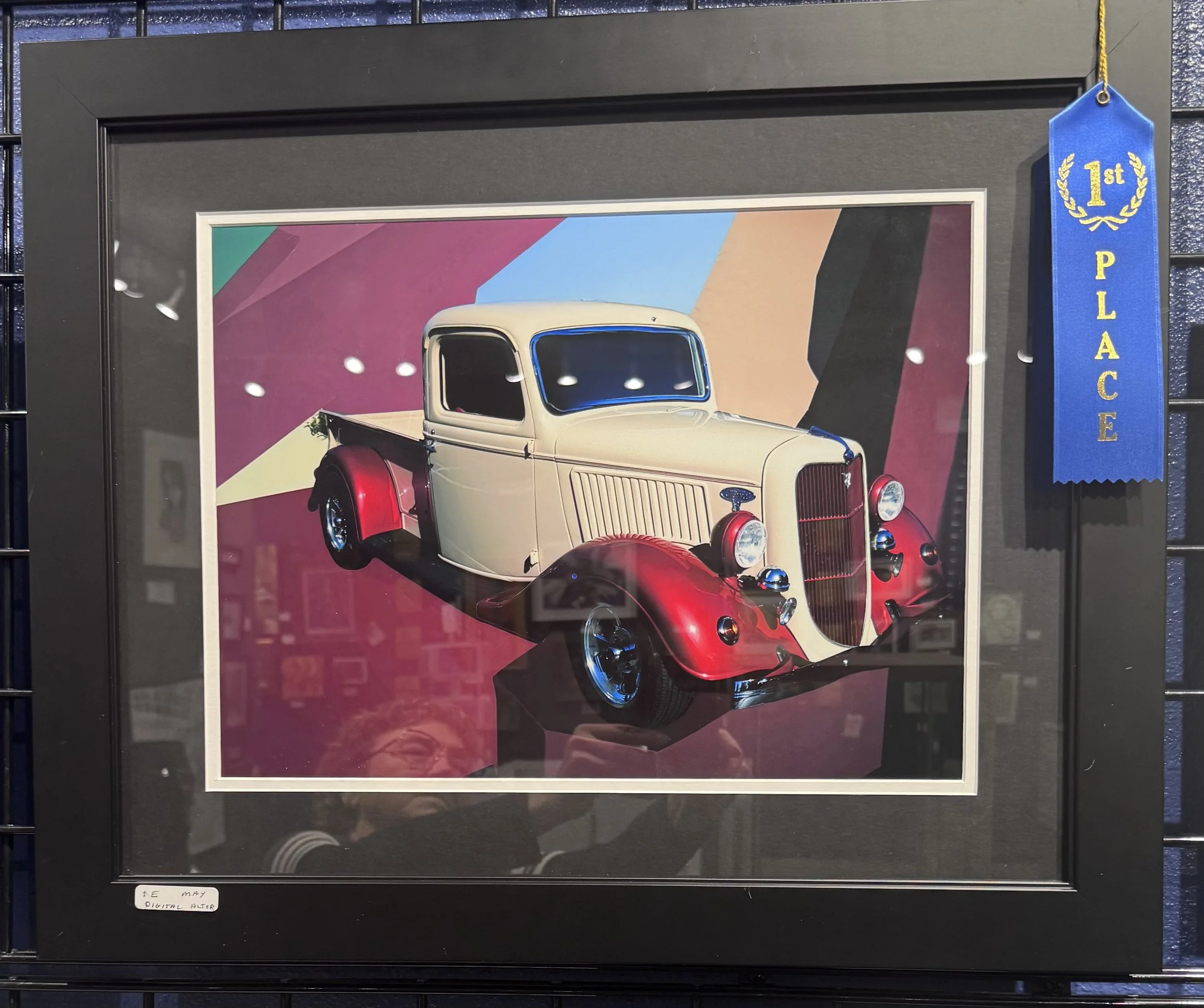 Framed digital poster of a vintage cream and red car with a colorful abstract background, displayed behind glass with reflections. Blue ribbon on right side indicating first place.