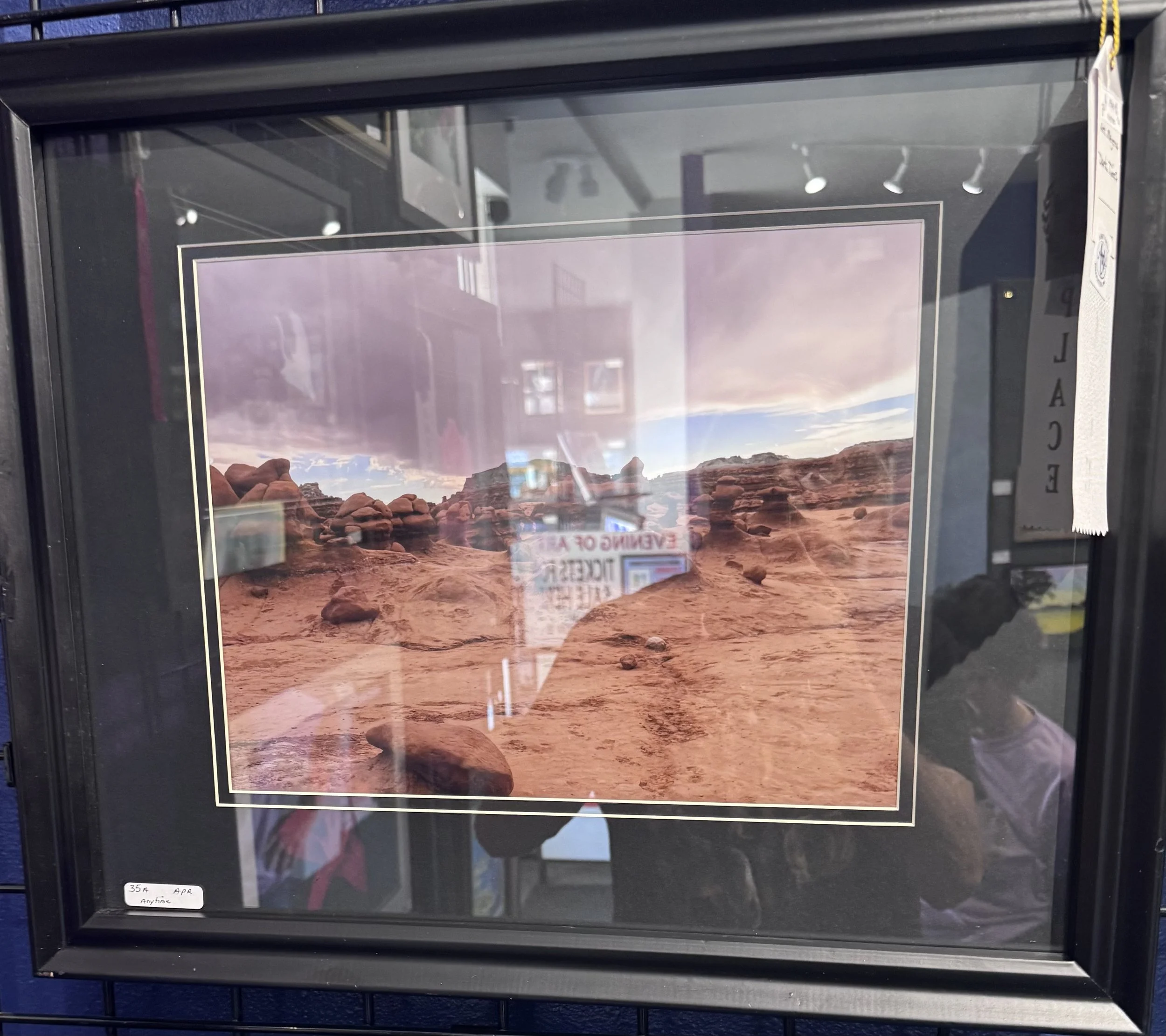 A framed landscape photograph of rocky desert terrain with distant mountains under a partly cloudy sky, displayed on a store wall.