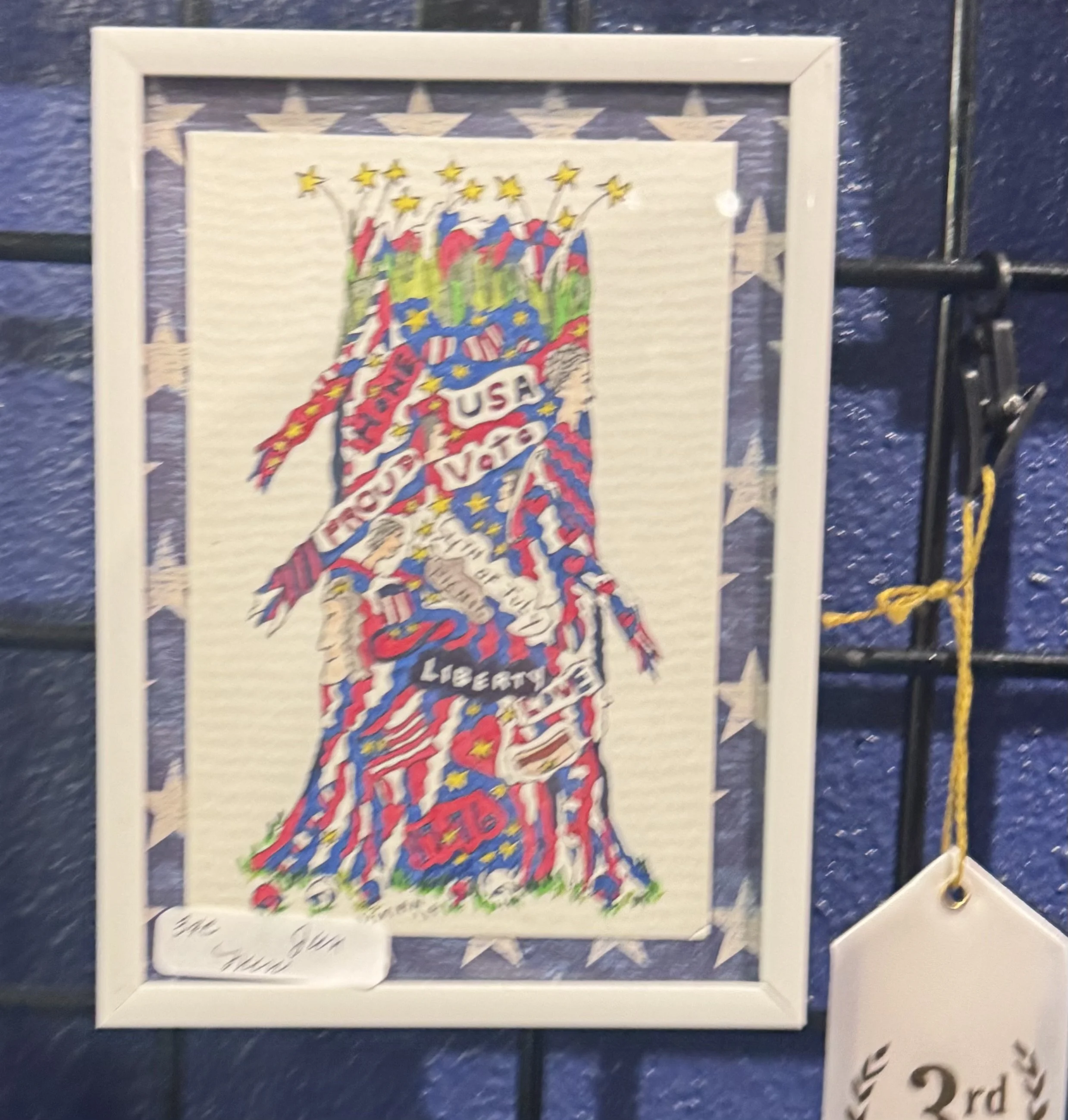 A framed cross-stitch embroidery piece showing the map of the United States decorated with stars, with the words "Freedom USA" written across the map, and colorful patriotic elements surrounding it.