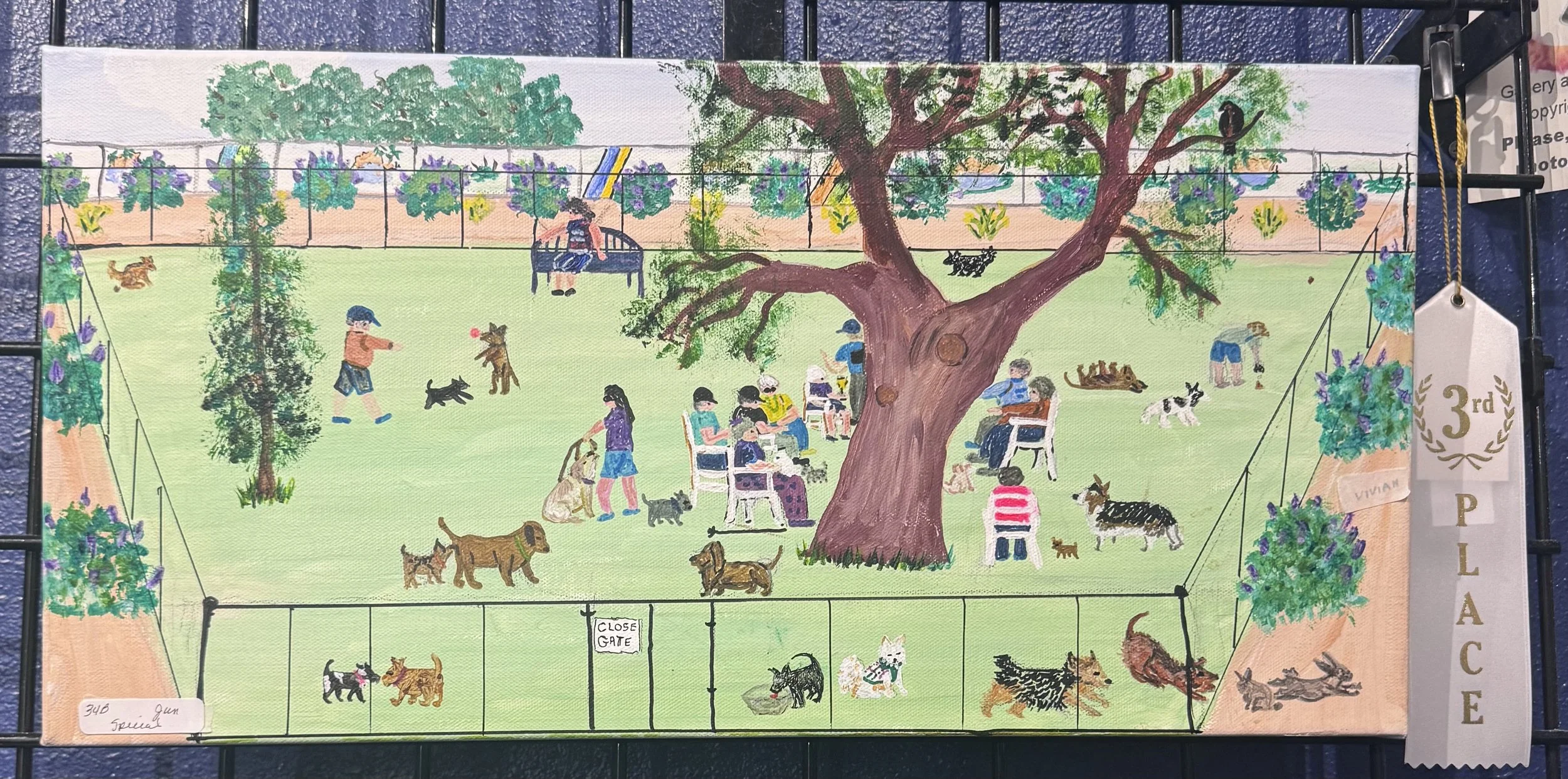 A colorful painting of a dog park scene featuring multiple dogs playing, people sitting on benches, and a large tree in the center, with a fence and greenery in the background.