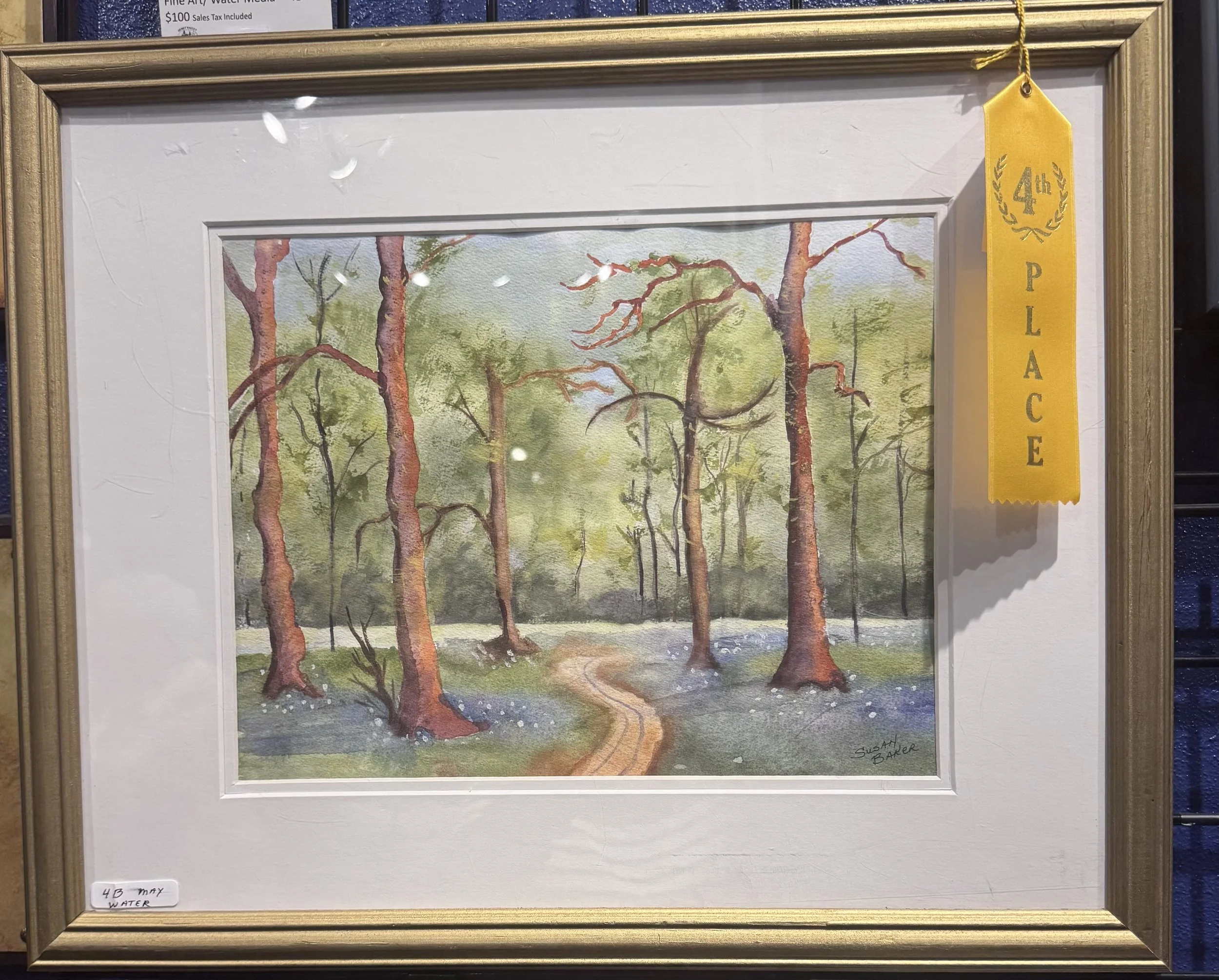 Watercolor painting of a forest path with trees, green foliage, and a winding dirt trail, signed by Susan Baker.