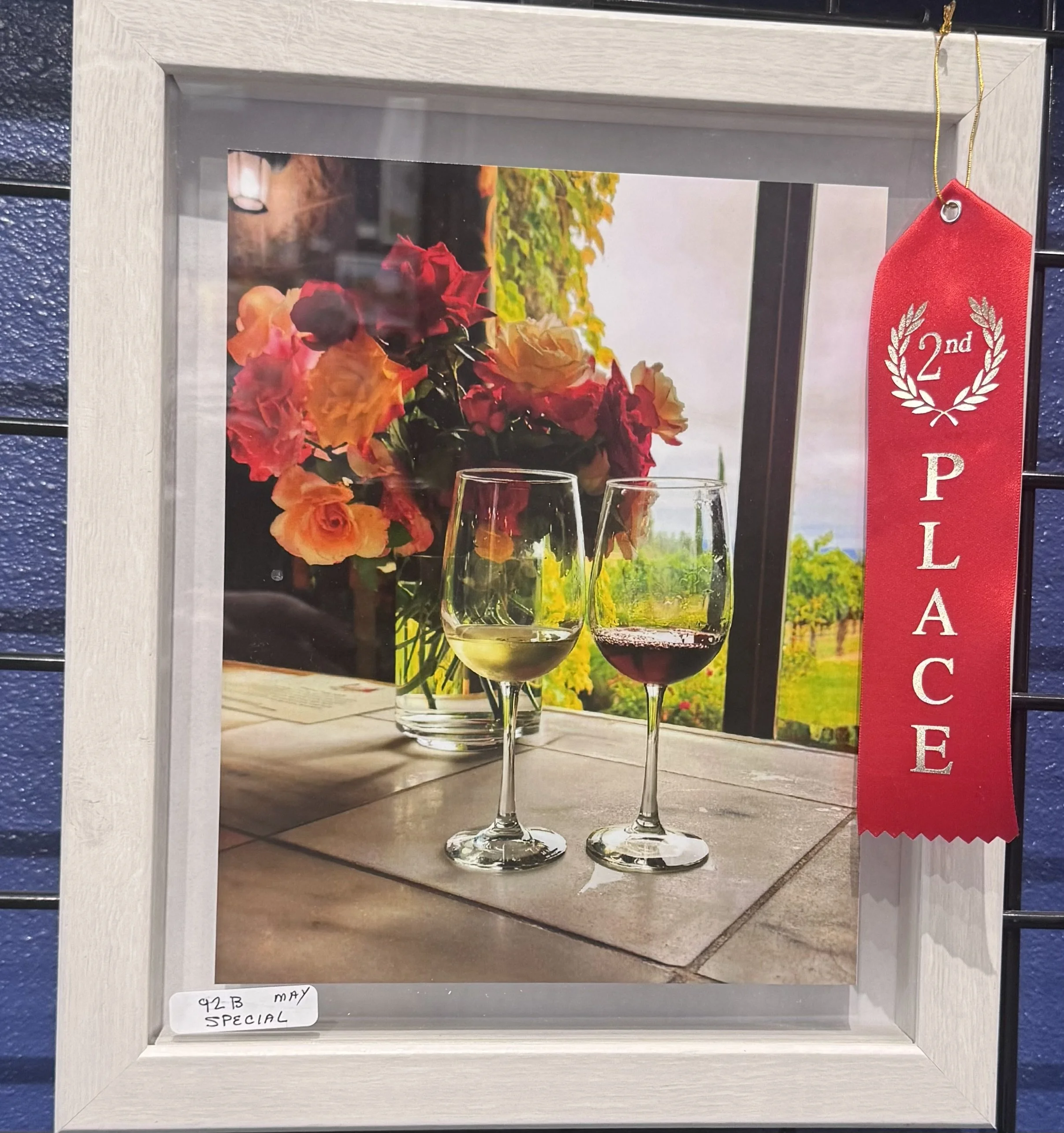 A framed photograph of a bouquet of orange and pink flowers and two glasses of white and red wine, with a vineyard in the background. A red ribbon on the right side reads '2nd PLACE'.