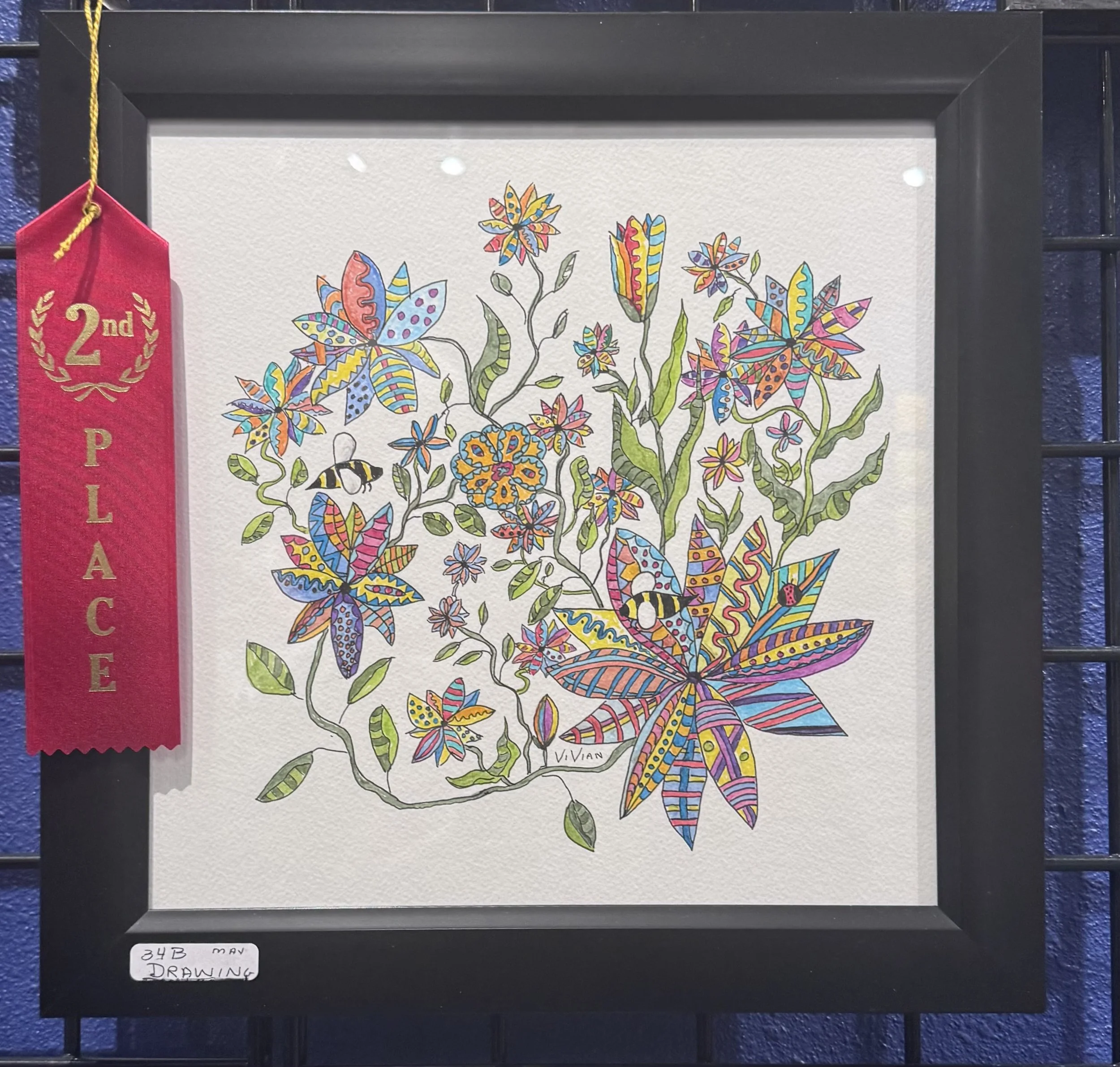 Colorful drawing of a butterfly and surrounding flowers on white paper, framed and displayed with a red ribbon marked '2nd place'.