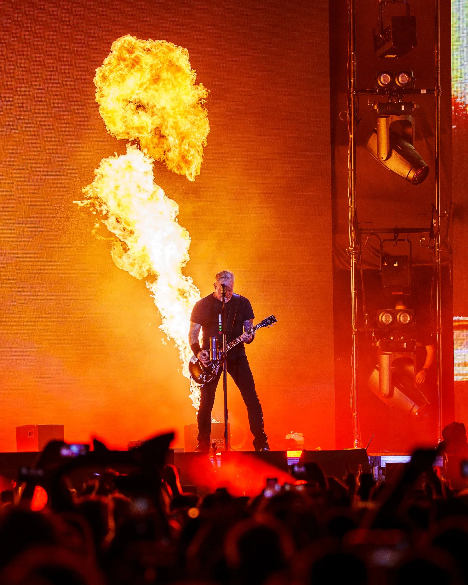 A musician playing an electric guitar on stage with fire effects behind him during a concert.
