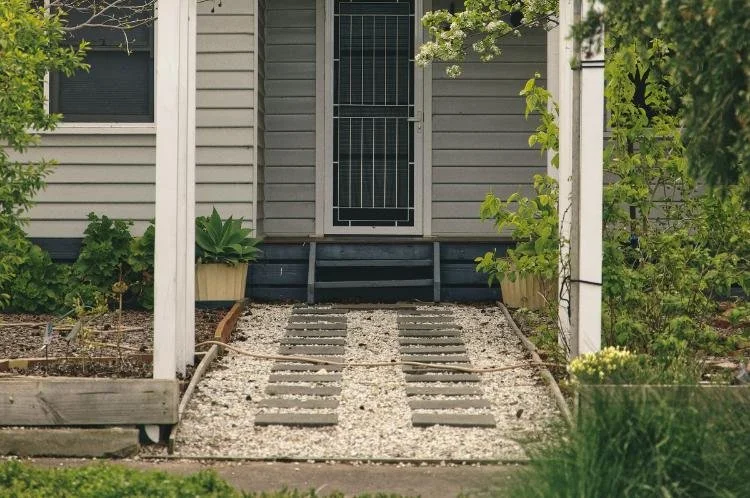 Gray pavers in white gravel leading up to short blue timber stairs, which sit below a white front door.