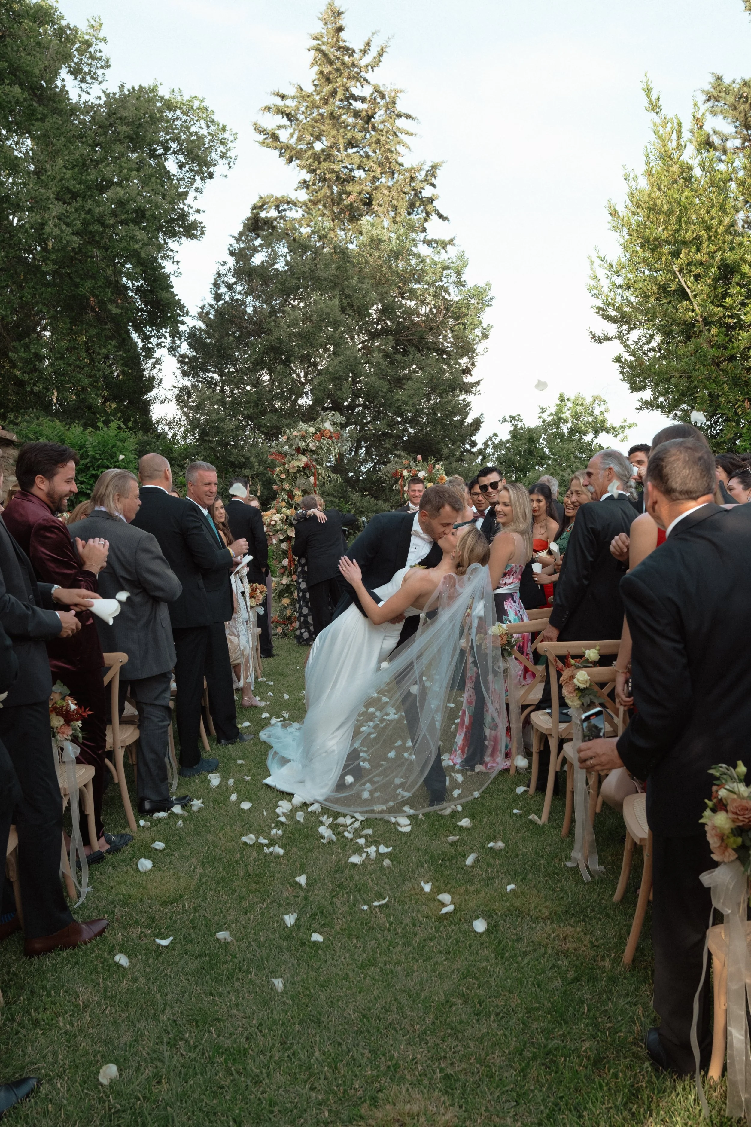 Romantic garden wedding ceremony at Castello di Bibbione in Tuscany, featuring the couple’s first kiss surrounded by guests, petals, and timeless Italian scenery.