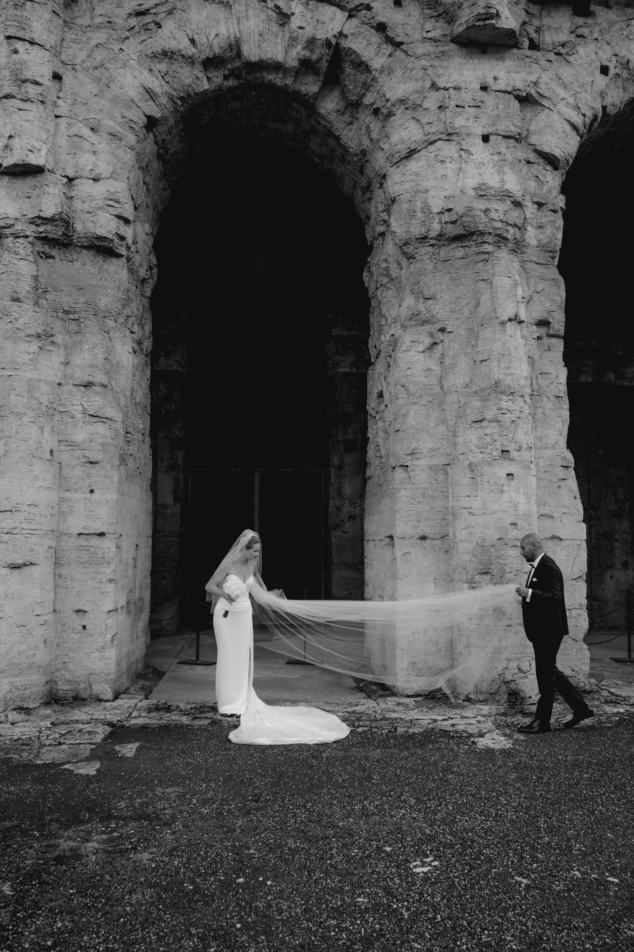 Black and white elopement portrait of a bride and groom beneath the Colosseum in Rome
