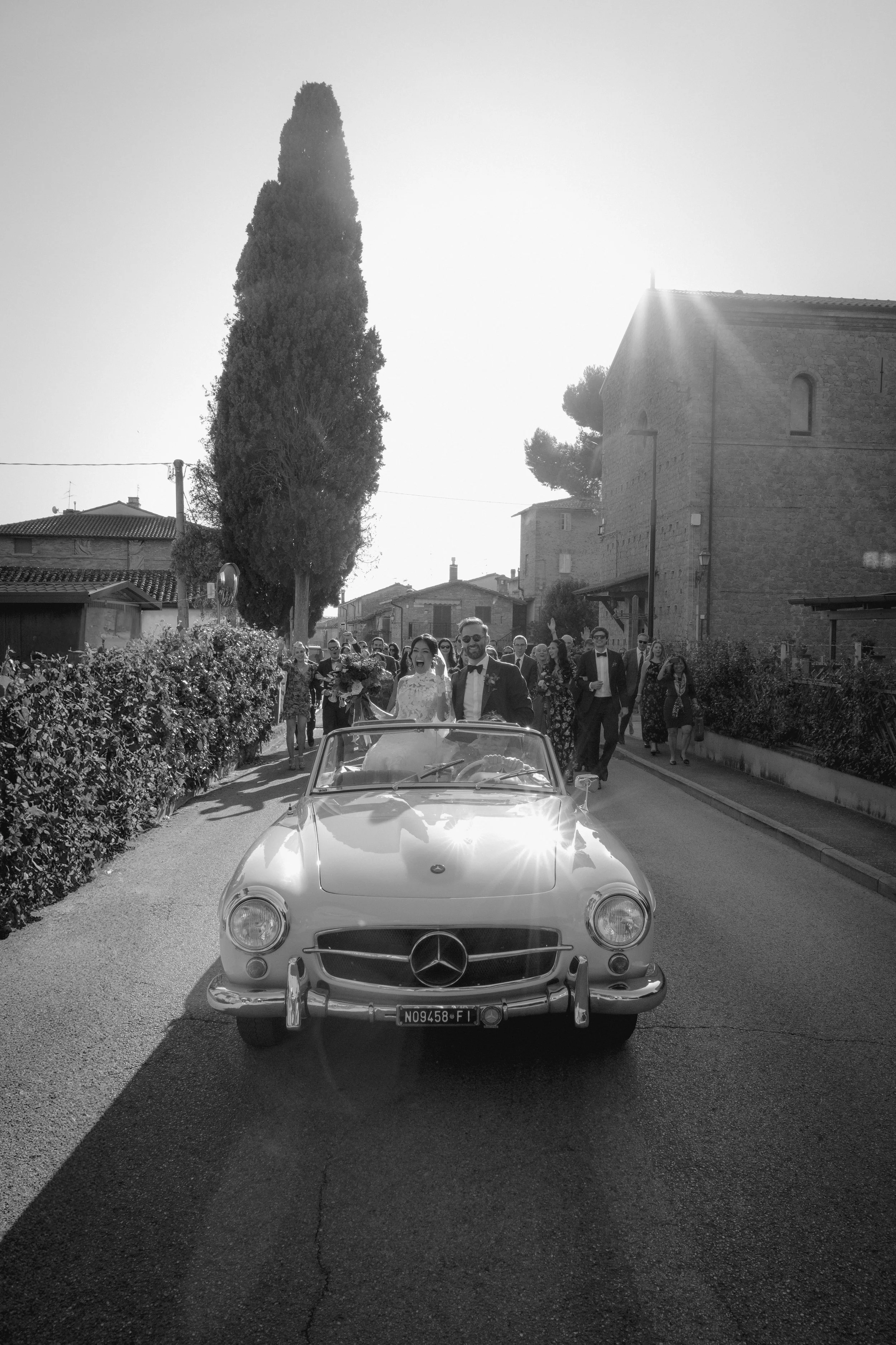 A joyful Tuscan wedding procession featuring a vintage car, celebrating tradition, landscape, and spontaneous emotion in the Italian countryside.