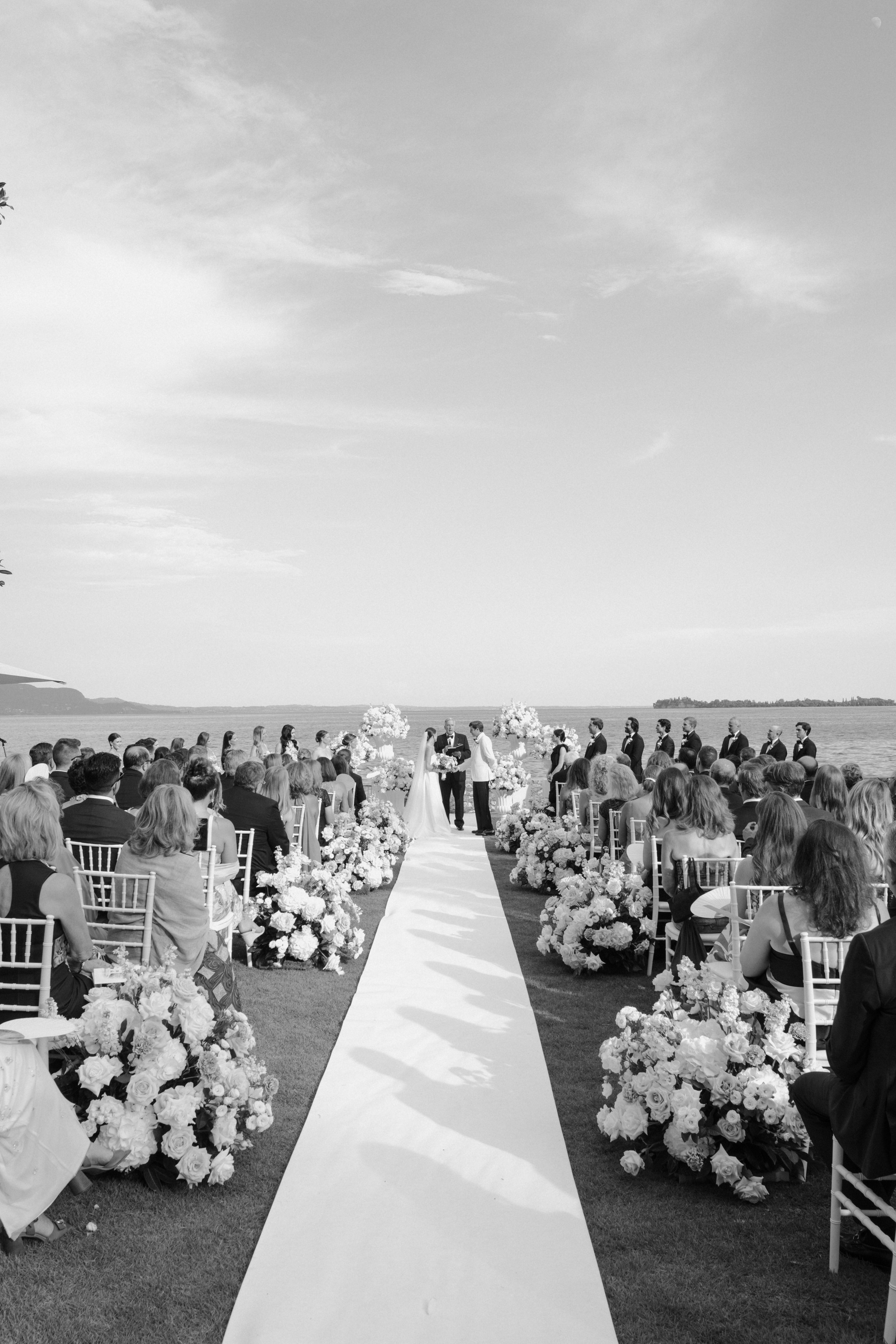 Elegant outdoor wedding ceremony with floral-lined aisle and lake views, set in a refined and exclusive Italian destination.
