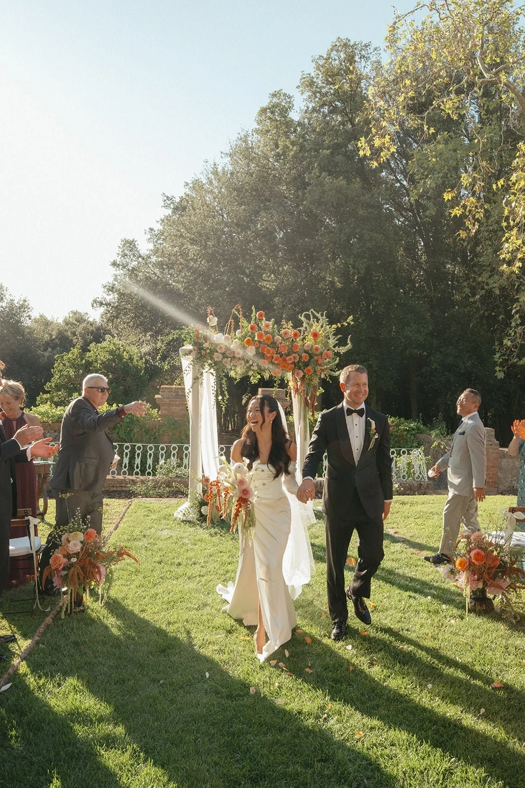 The bride and groom walk hand in hand down the aisle as guests applaud, marking the joyful end of their ceremony at Villa Lena.
