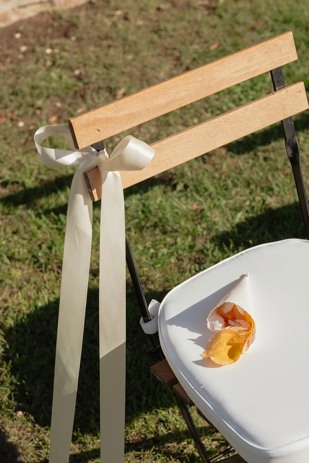 A close detail of a wooden ceremony chair adorned with soft ribbon and flower petals, captured in warm Tuscan light.