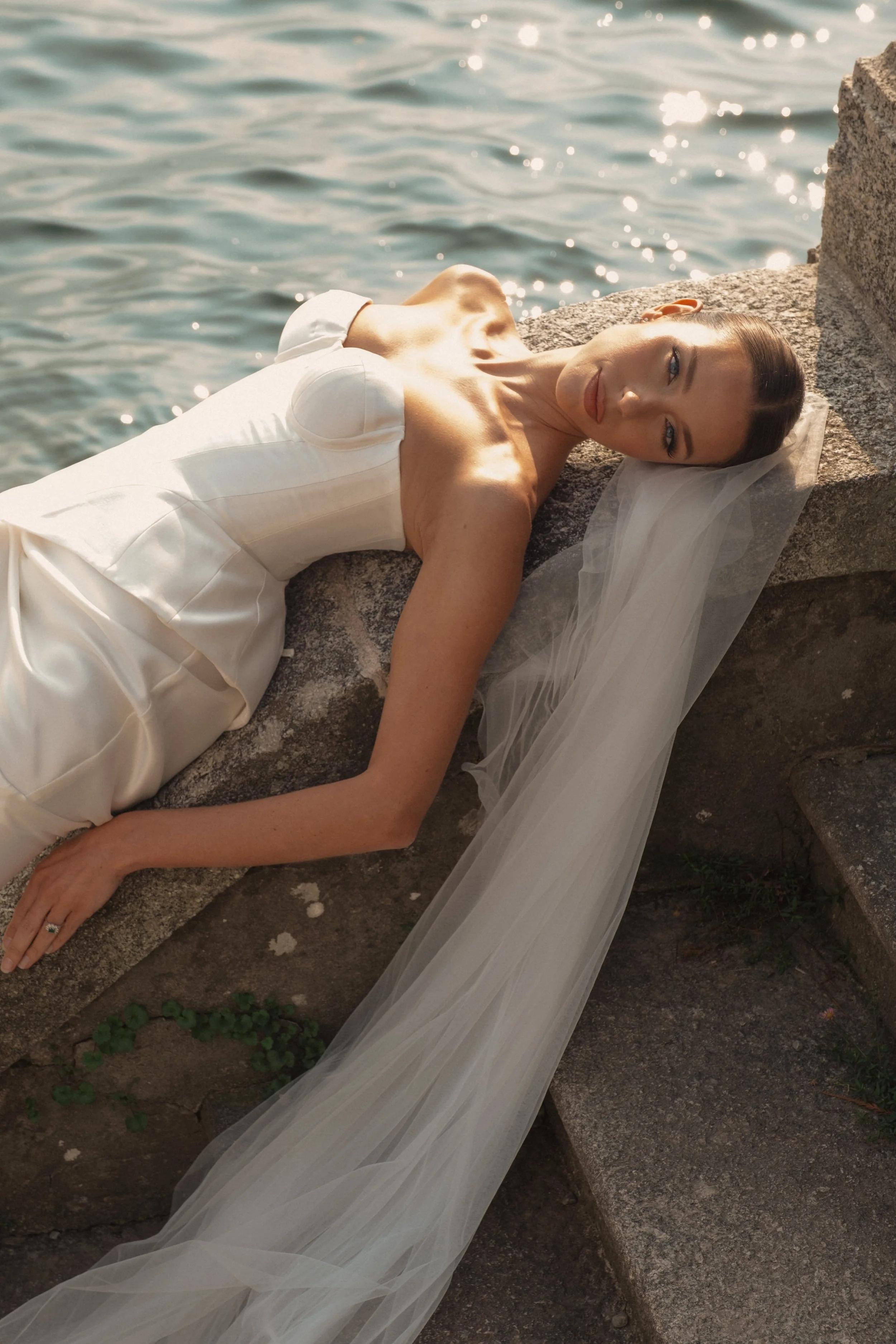 An editorial bridal portrait on Lake Como, featuring a modern satin gown and veil, photographed in soft natural light with a fashion-inspired approach.