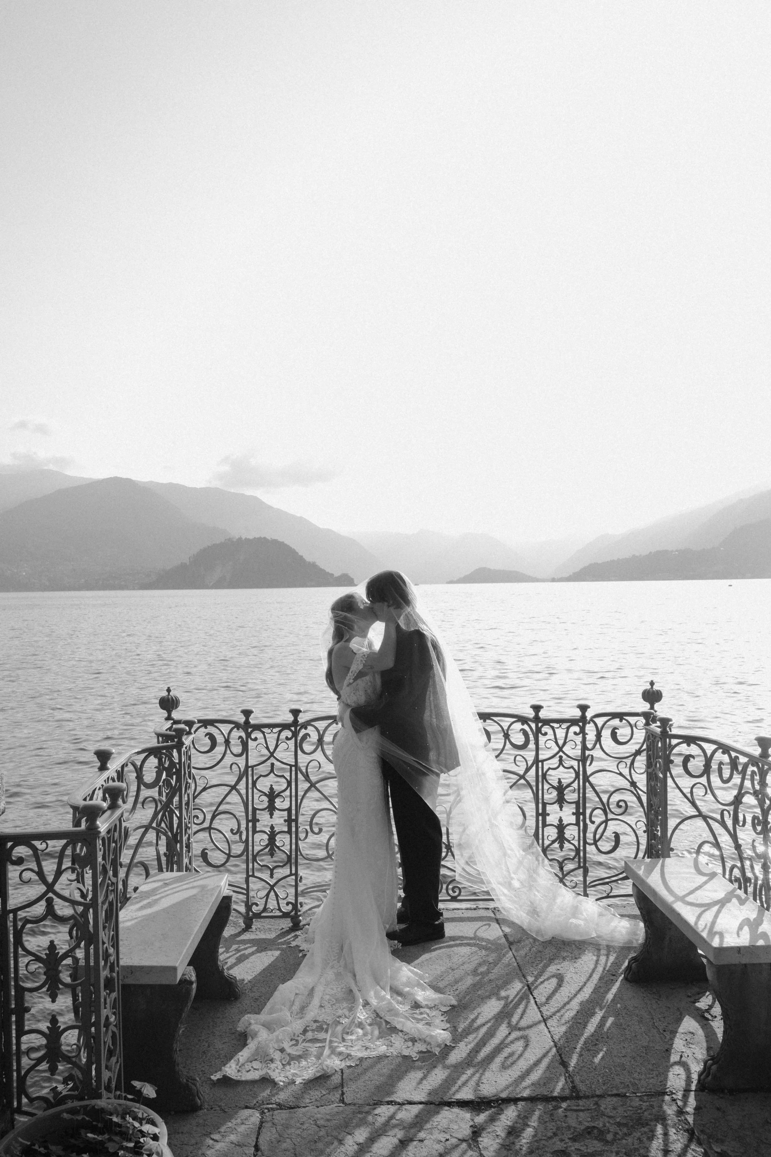 Bride and groom kissing on a terrace at Villa Monastero overlooking Lake Como in Varenna, Italy.
