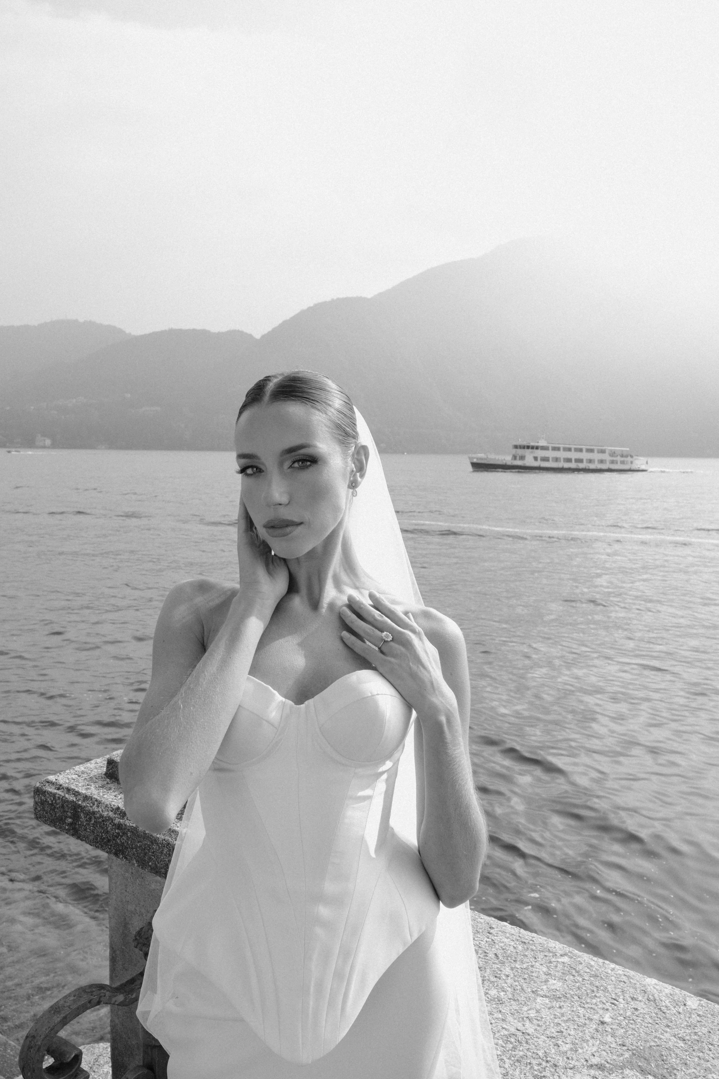 A refined editorial bridal portrait on Lake Como, capturing modern elegance and timeless beauty as the bride poses by the water in a minimalist corset gown, framed by the serene Italian landscape.