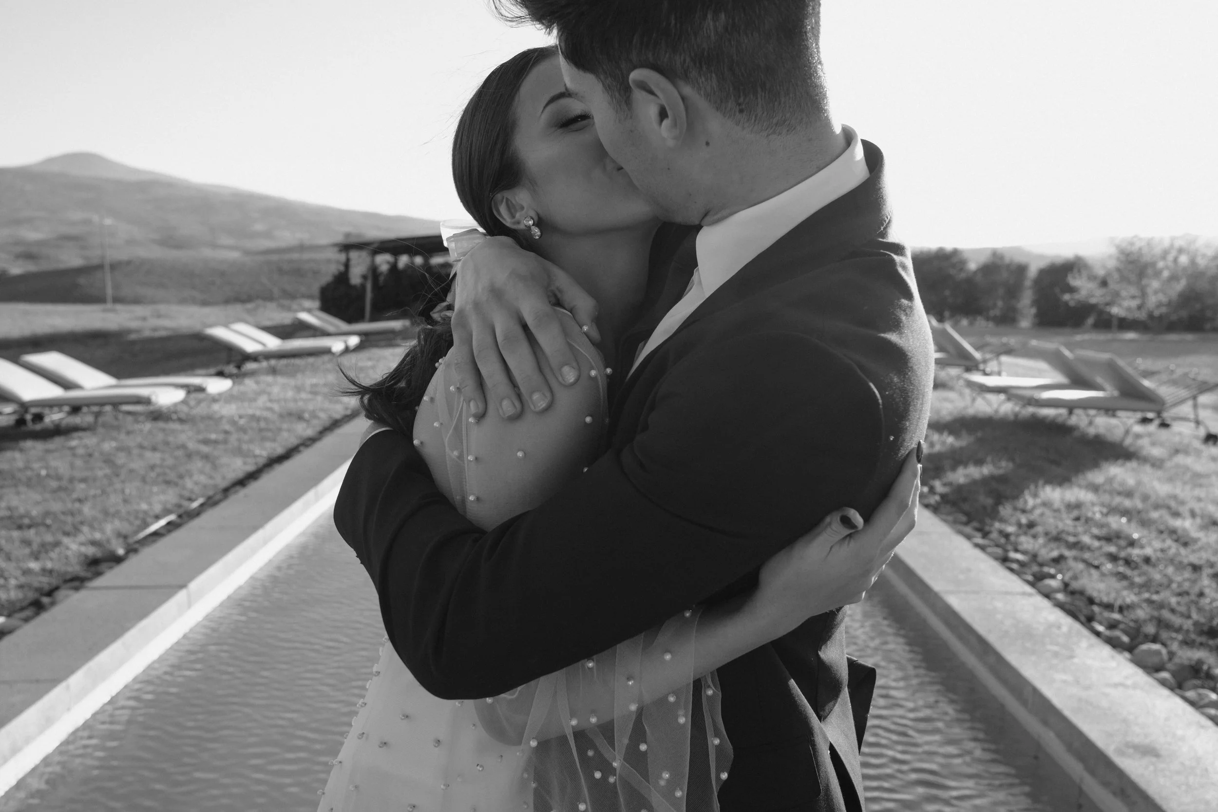 An intimate, documentary-style moment from a bespoke wedding in Tuscany, capturing a couple’s quiet embrace amid the soft landscapes of the Val d’Orcia—refined, emotional, and timelessly Italian.