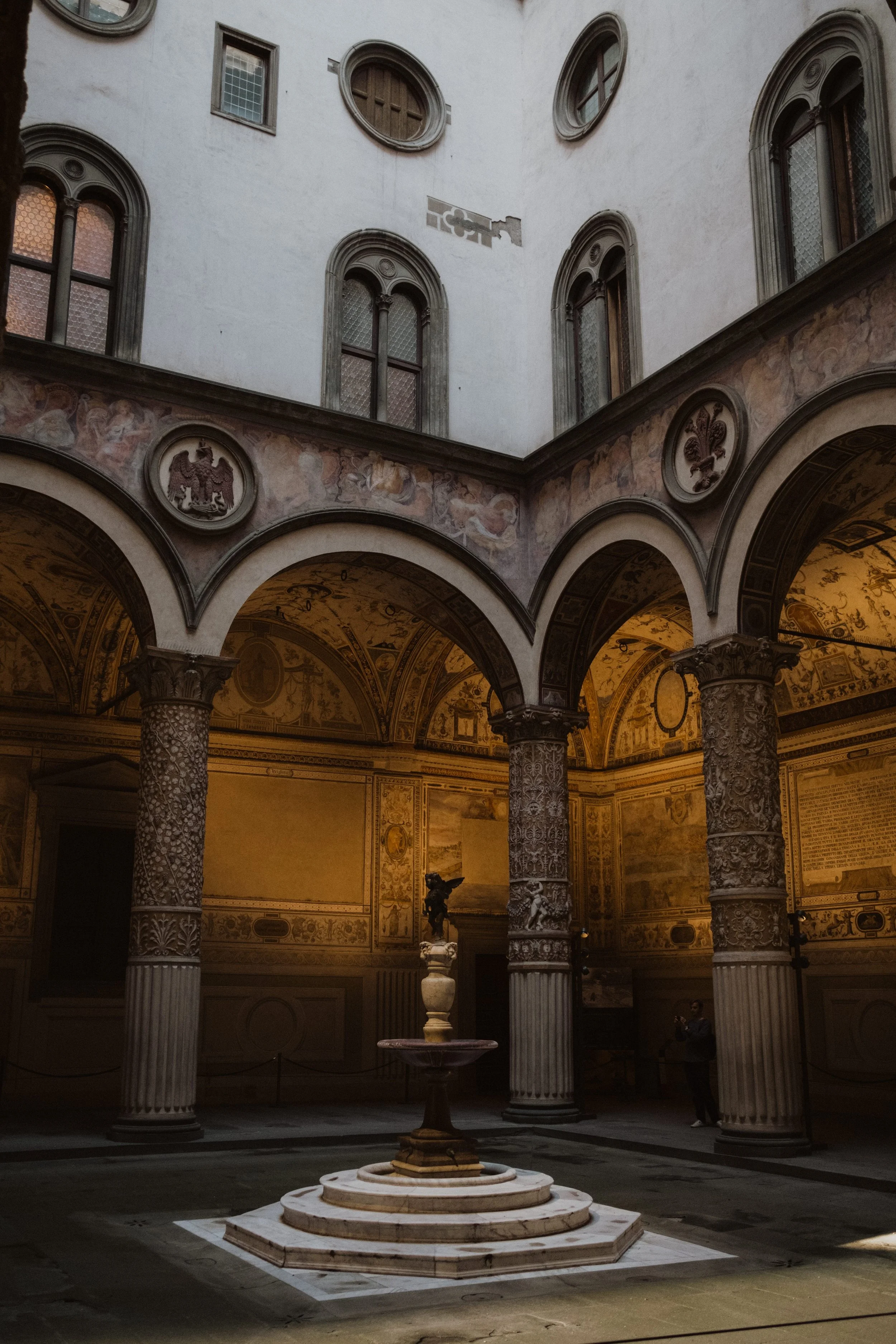Historic Florentine courtyard with ornate arches, frescoed walls, and a central fountain, illuminated by soft natural light in the heart of Florence, Italy.