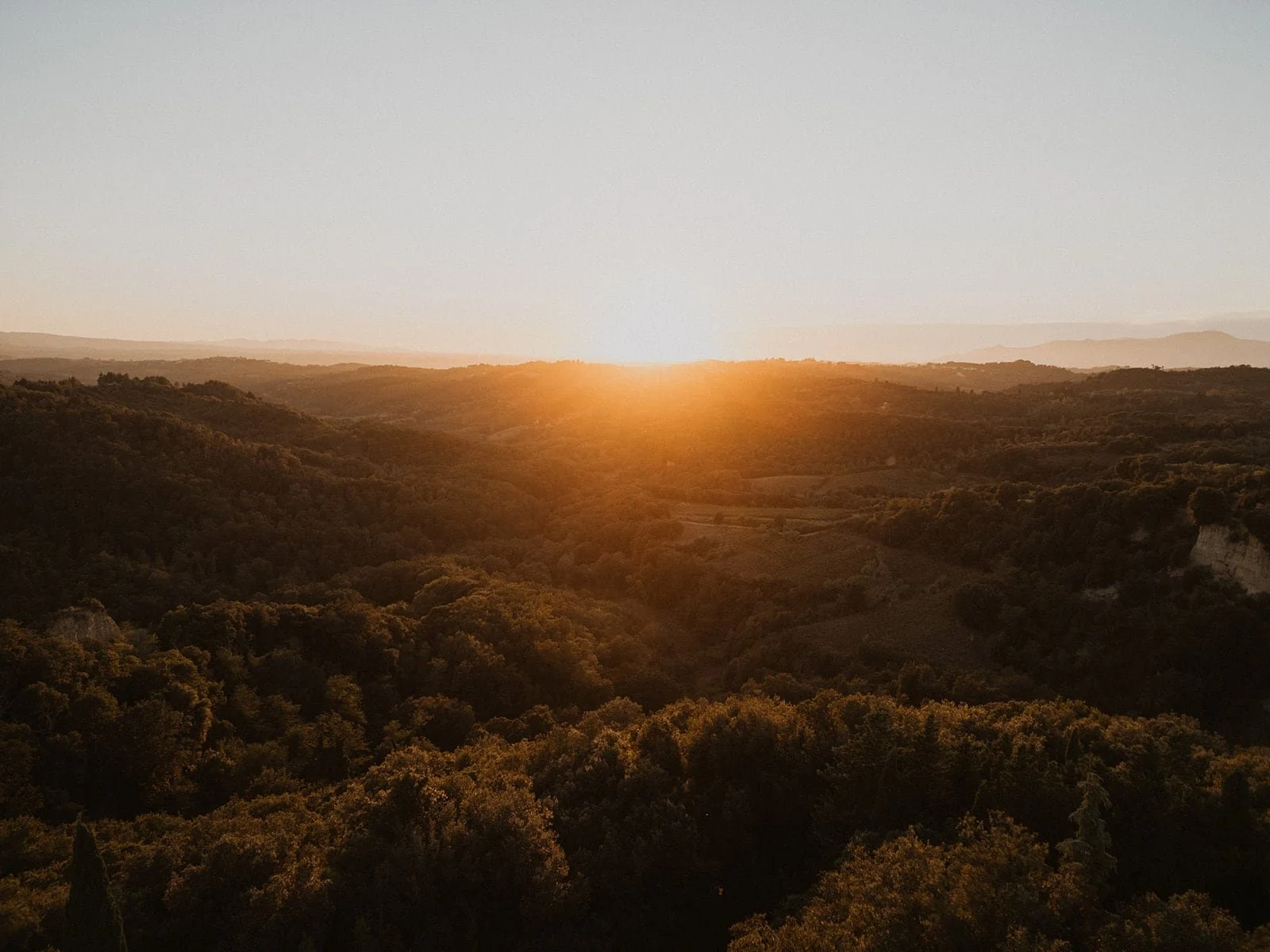 A landscape photograph of the rolling hills and dense forests surrounding the venue, captured during a hazy, golden sunset.