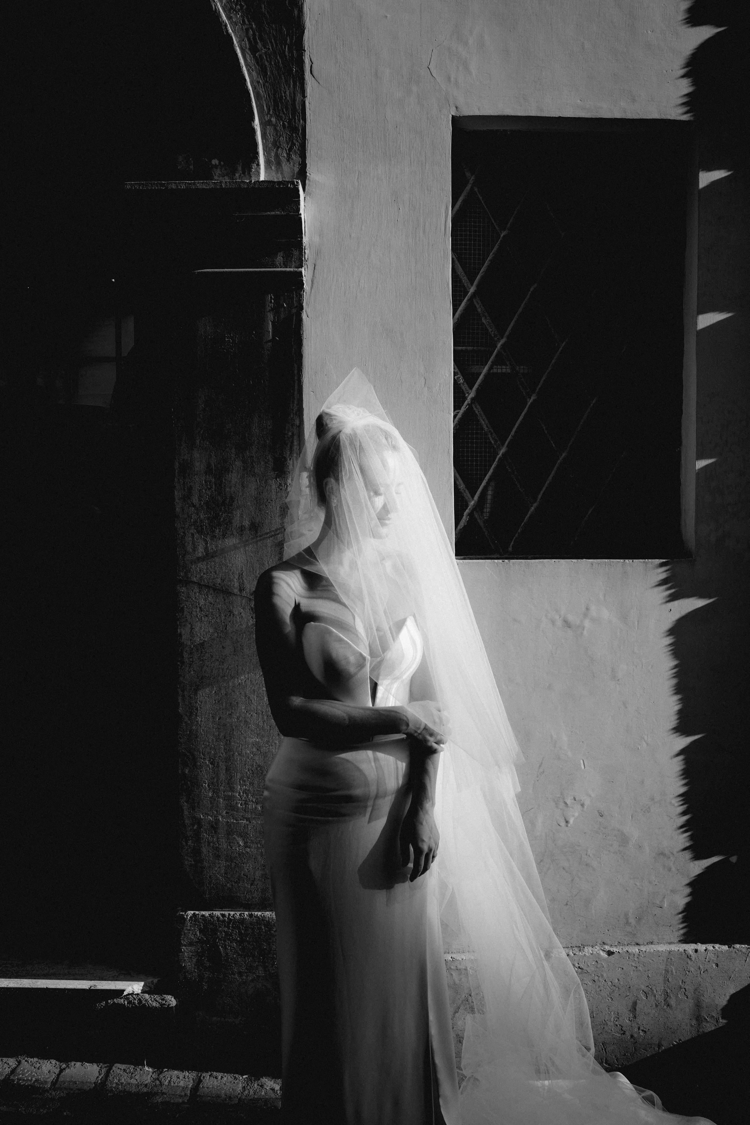 An artistic black and white bridal portrait in Rome, where soft light and deep shadows shape an intimate moment beneath the bride’s veil.