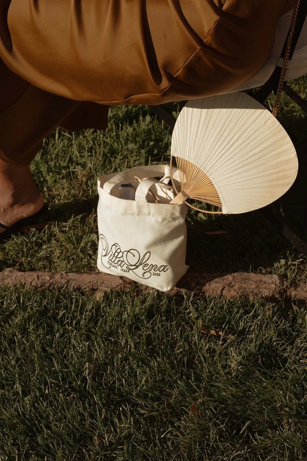 A still life of a guest’s folding fan and tote bag resting on the grass, captured during the summer wedding ceremony in Tuscany.