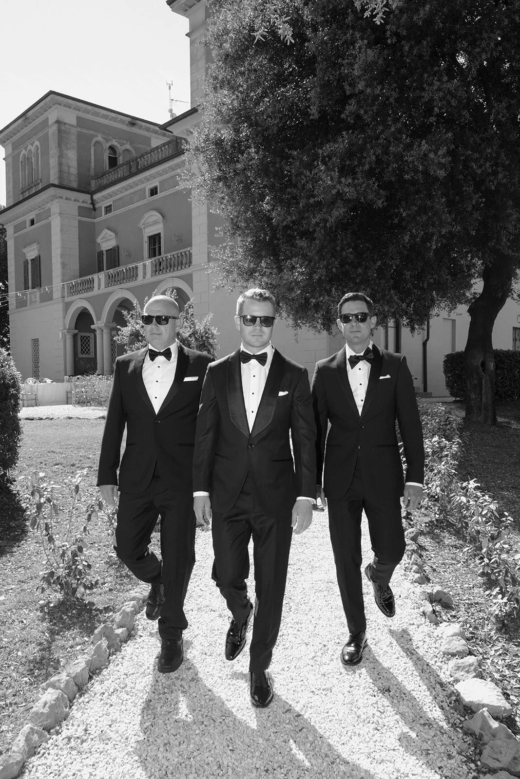 The groom walking with his groomsmen through the gardens of Villa Lena, photographed in a classic black and white style.